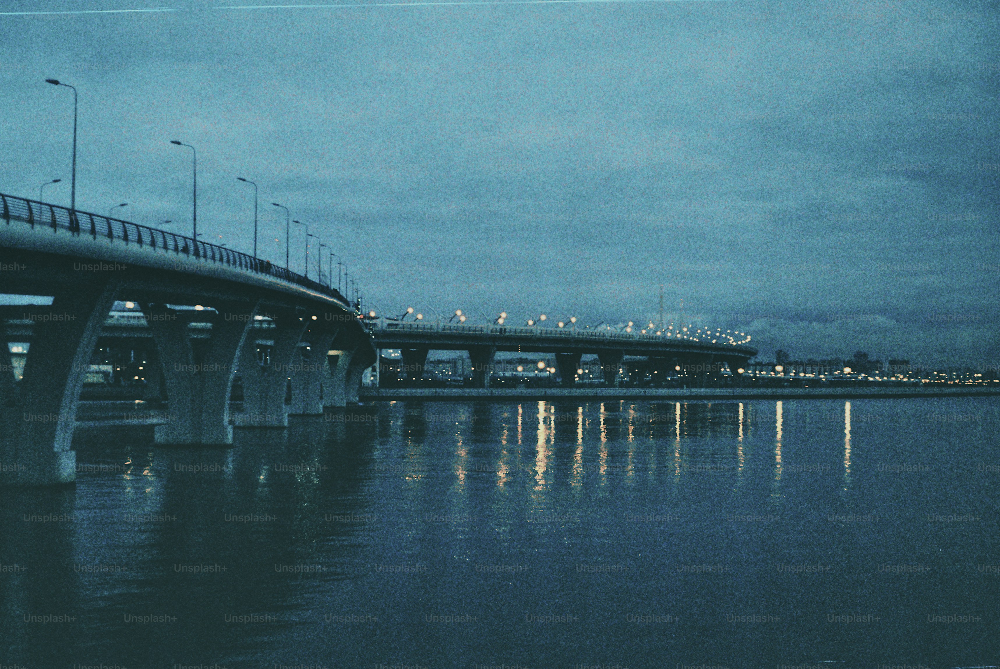Bridges over water at dusk with city lights reflected.