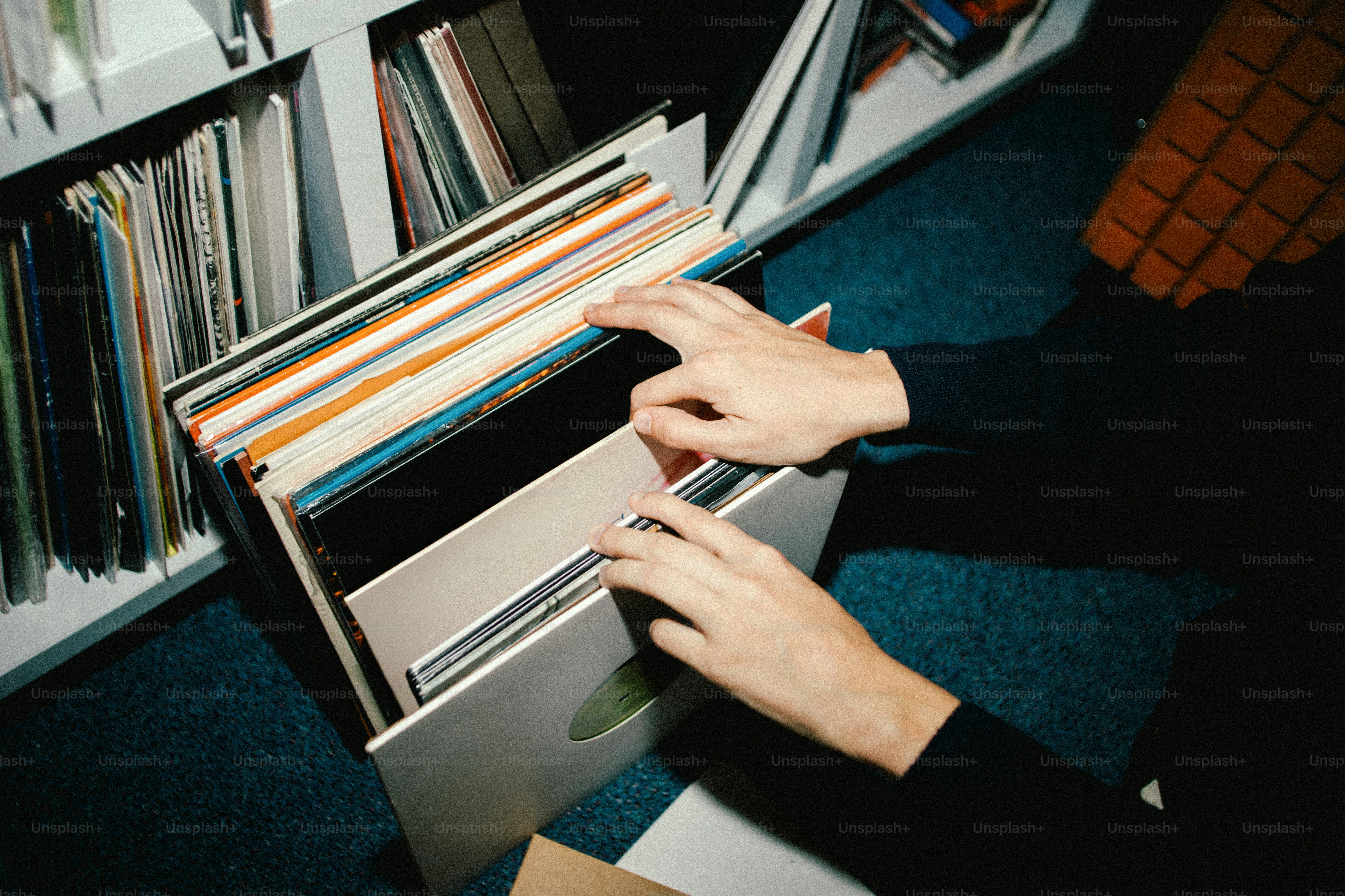 Hands sorting through vinyl records on a shelf.