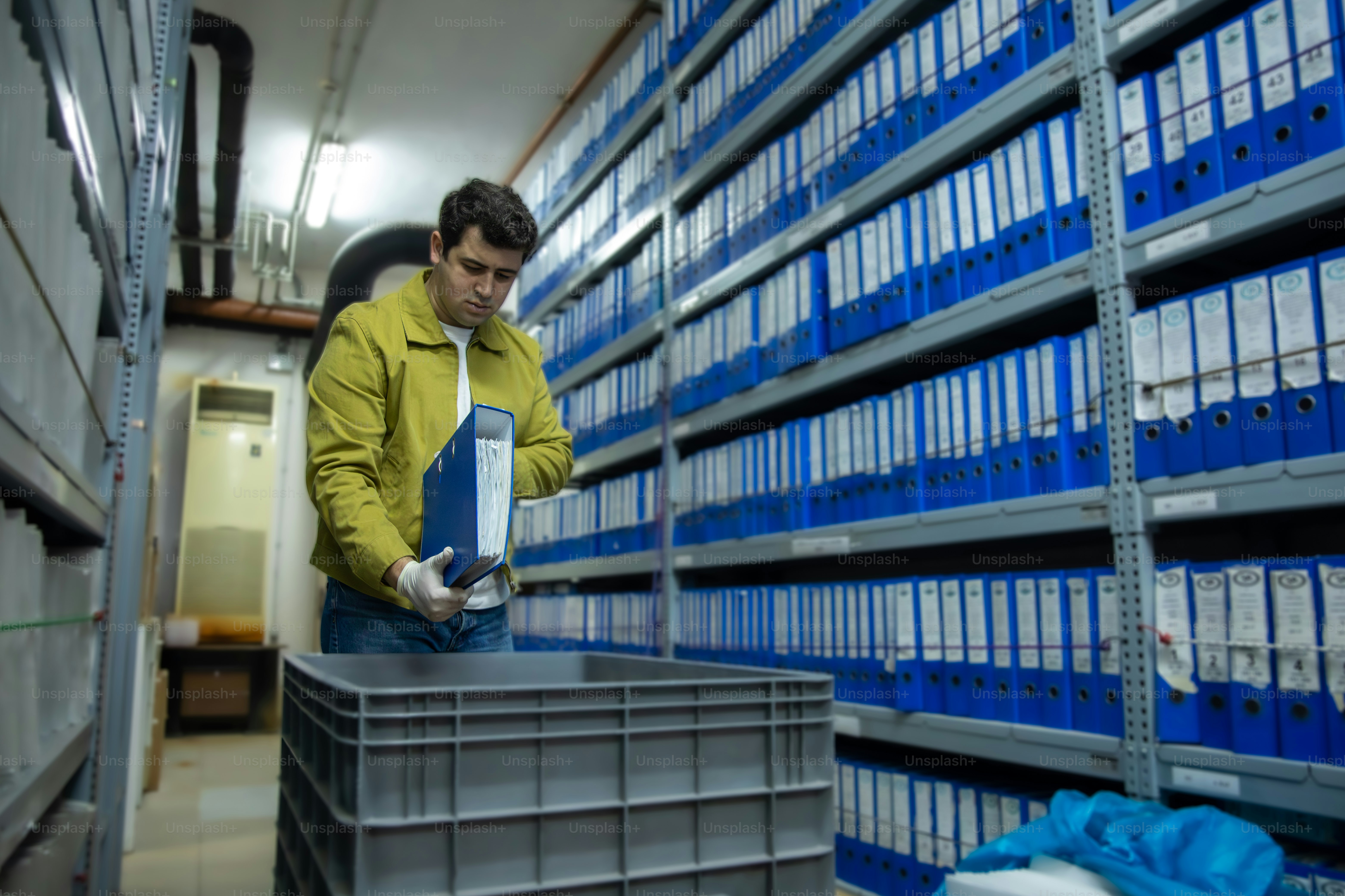 노란 재킷 입은 남자가 창고에서 서류를 정리하고 있어.