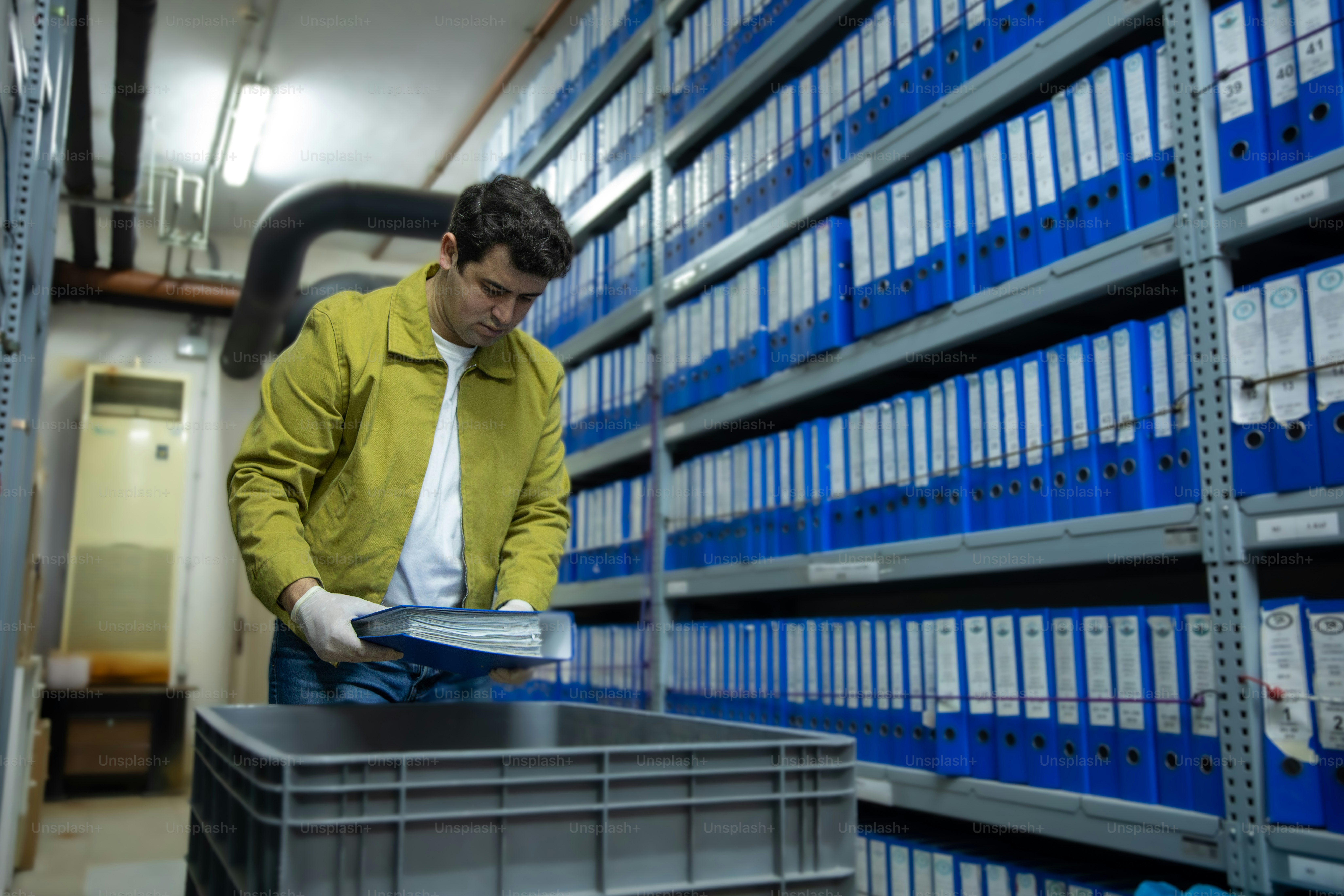 노란 재킷을 입은 남자가 기록실에서 파일을 분류하고 있다