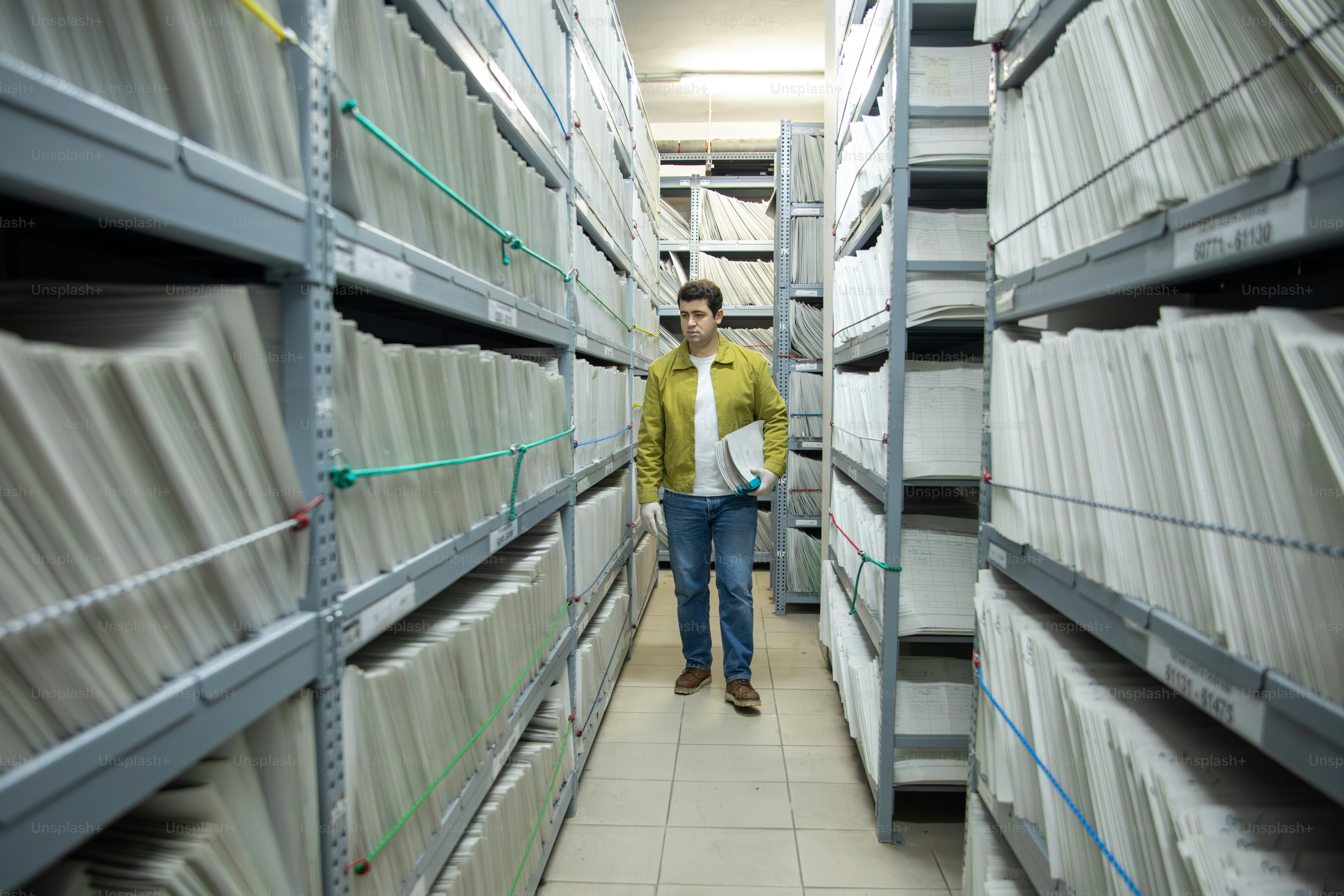 기록 보관소 파일 선반 사이를 걸어 다니는 남자.