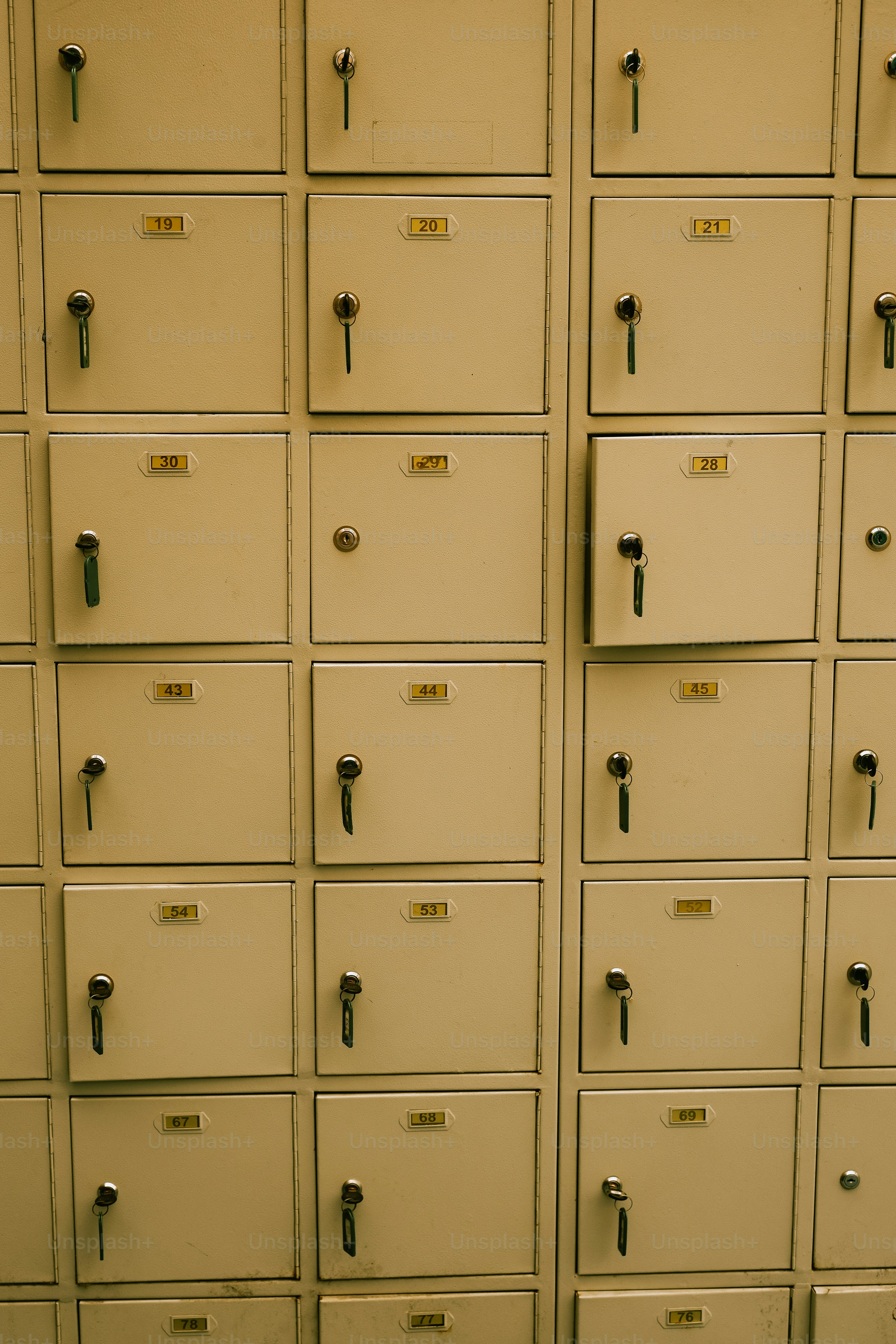 A wall of beige lockers with keys in locks.