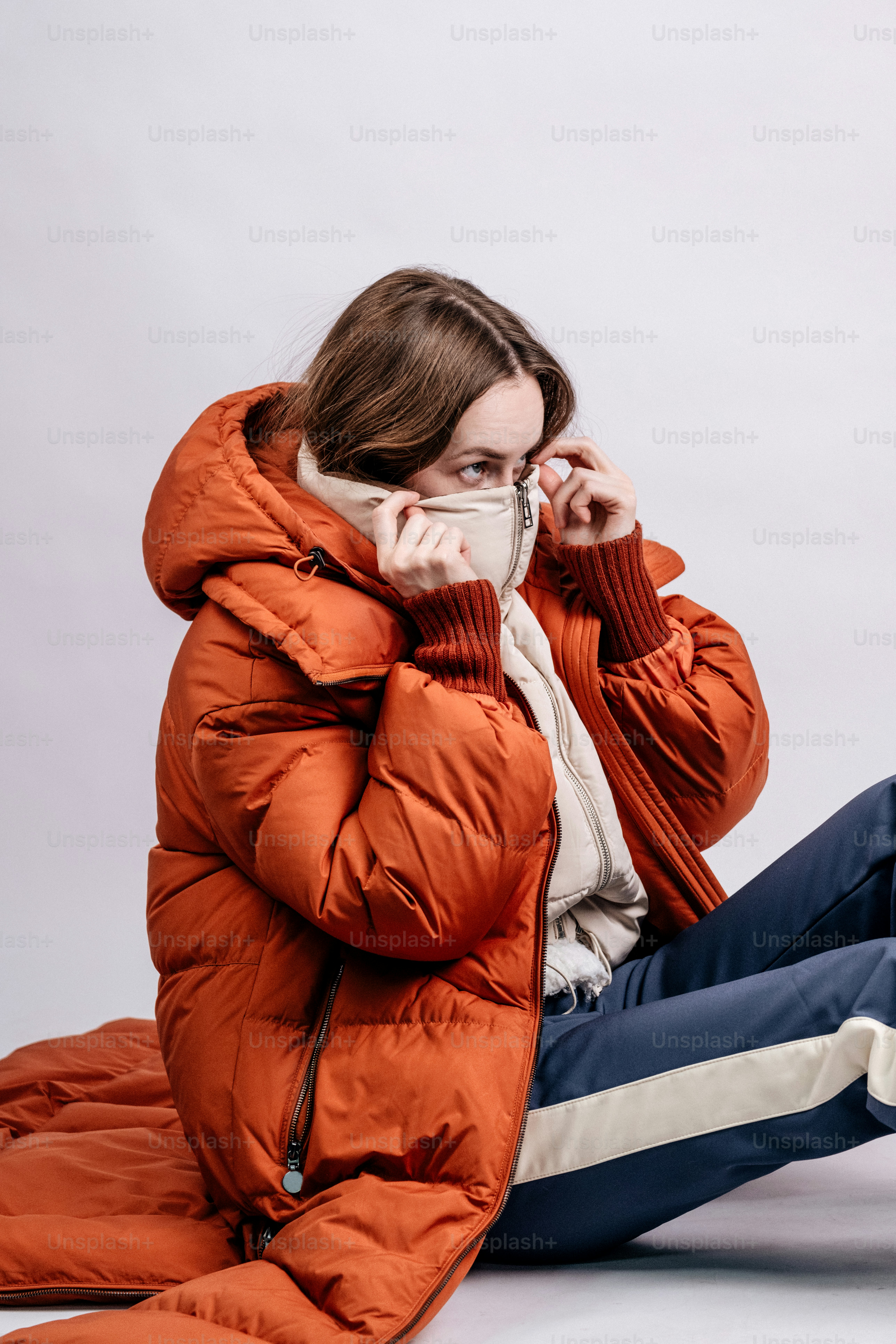 Woman in orange puffer jacket adjusts her scarf.