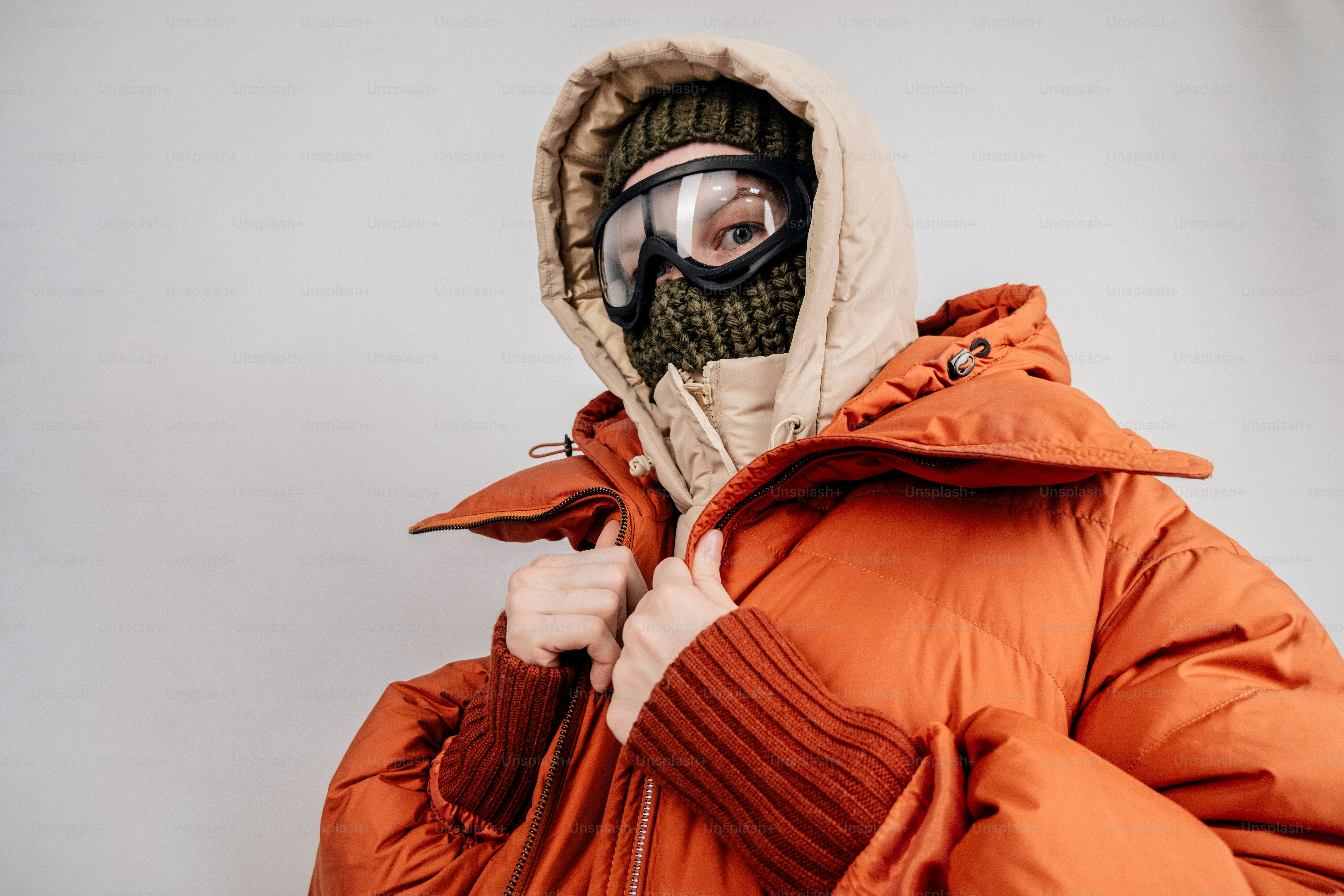 Person in Winterkleidung mit Schutzbrille und orangefarbener Daunenjacke