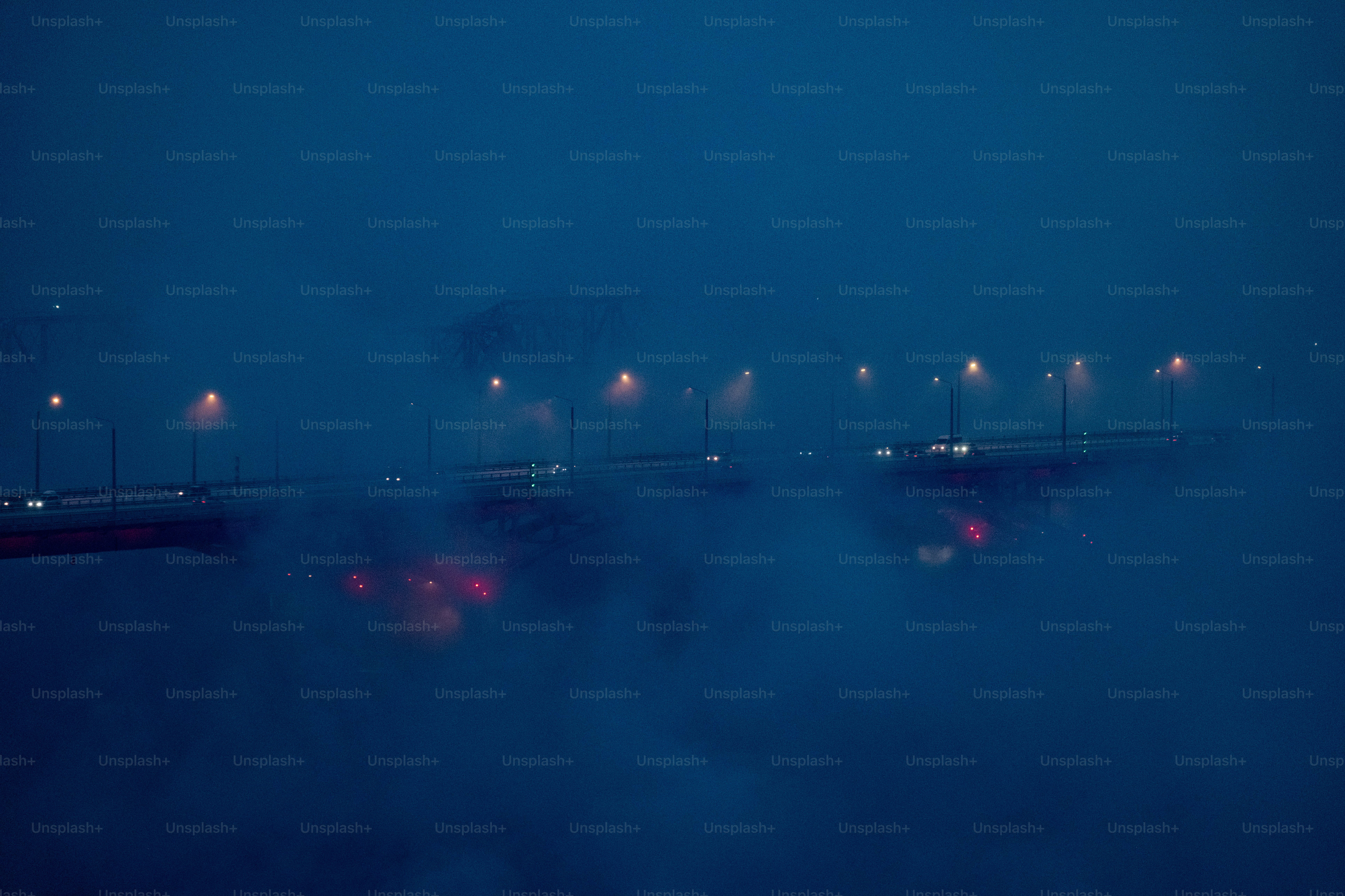 Streetlights illuminate a foggy bridge at night.