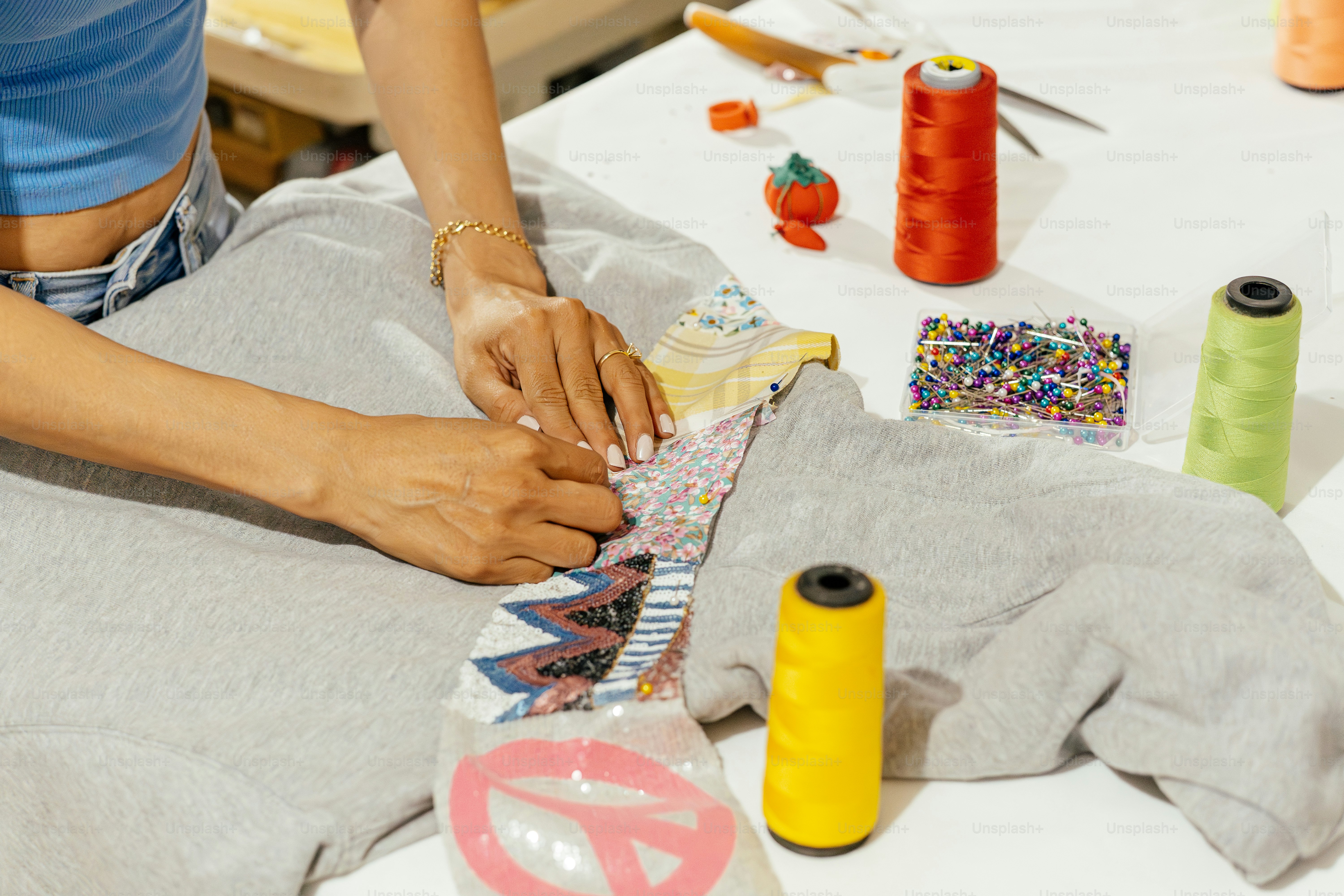 Hands sewing a colorful patch onto grey fabric