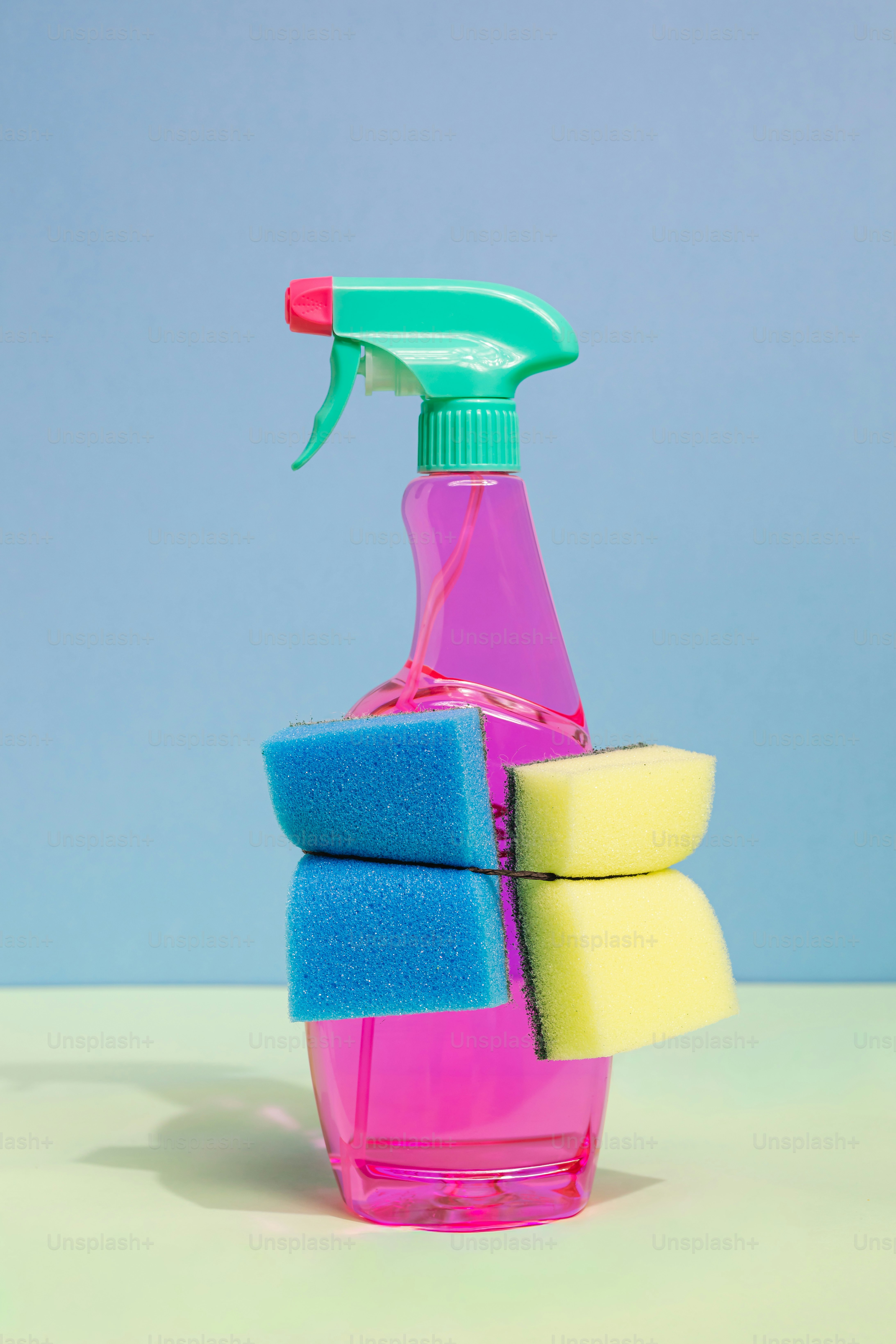Pink spray bottle with sponges on a pastel background