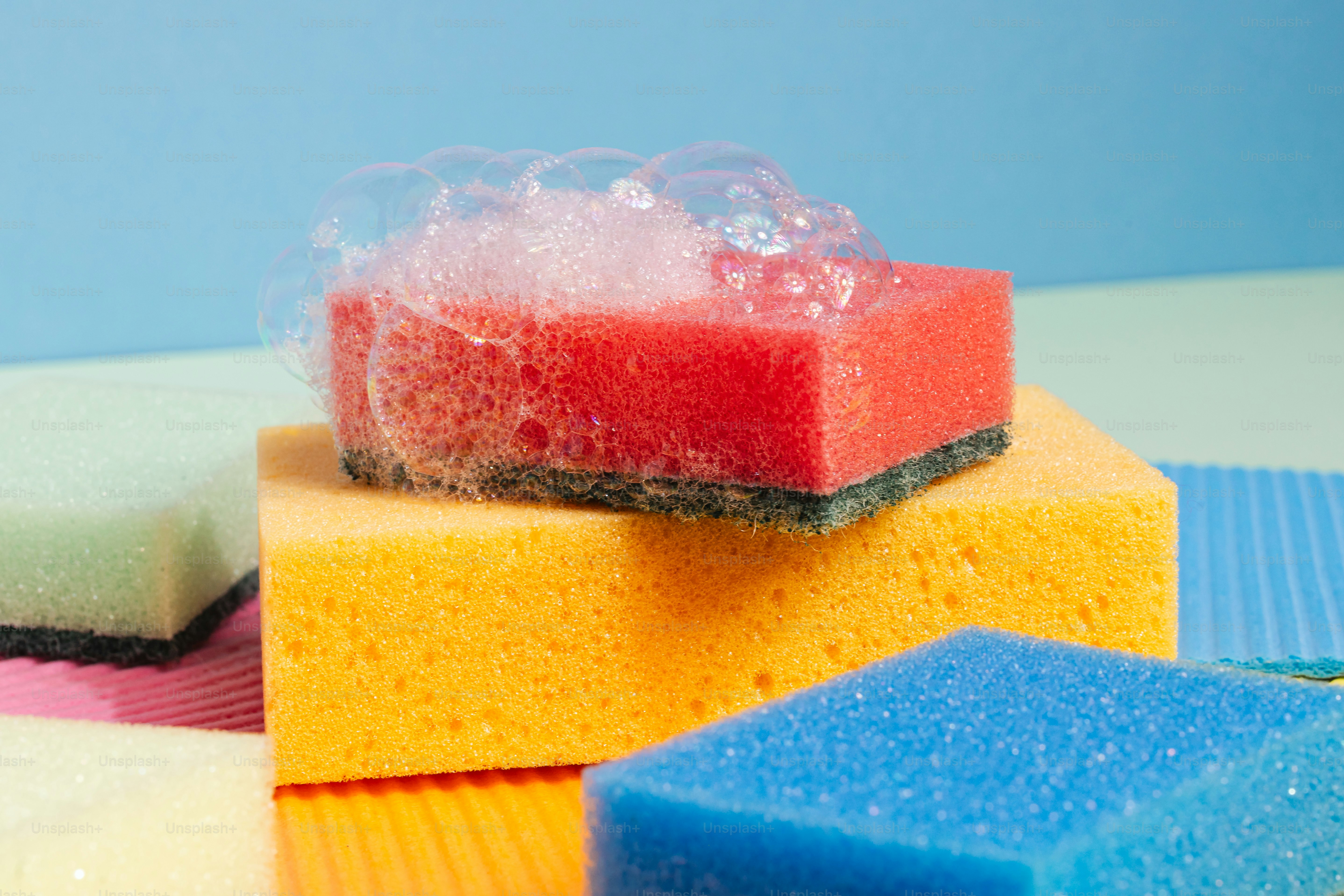 Colorful sponges with soap bubbles on a pastel background
