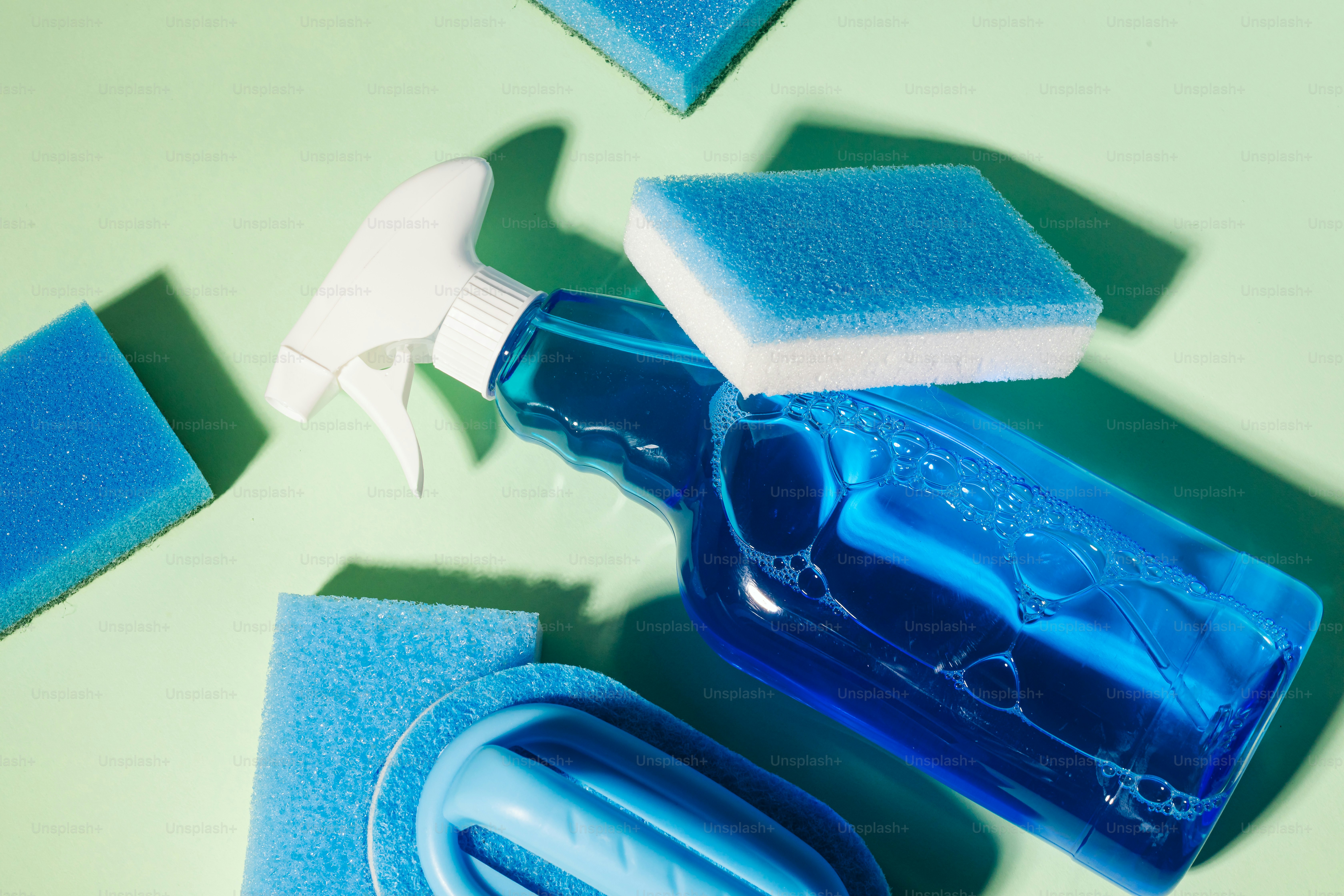 Blue cleaning spray bottle with sponges on light green background