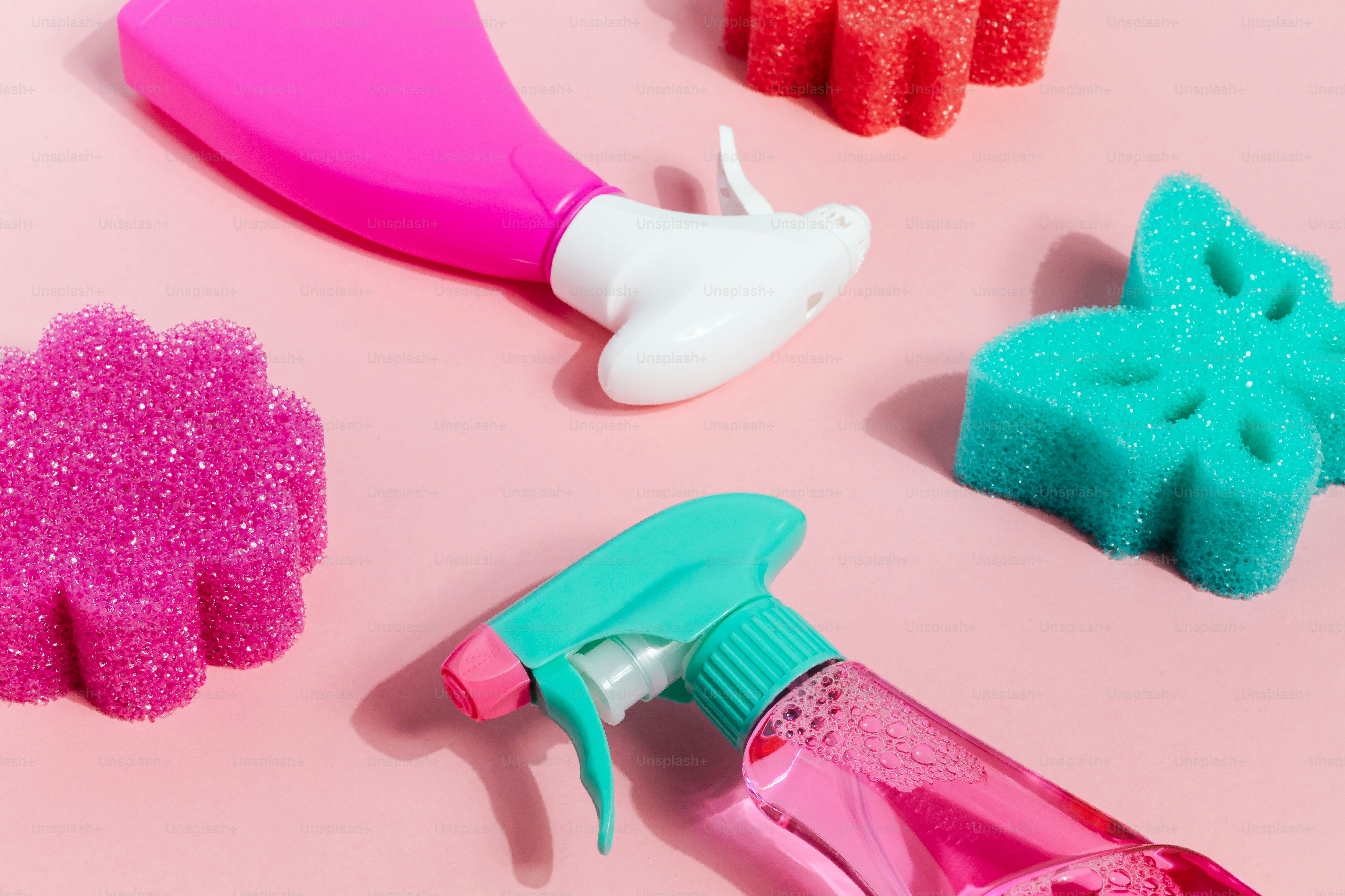 Colorful cleaning supplies and sponges arranged on pink background