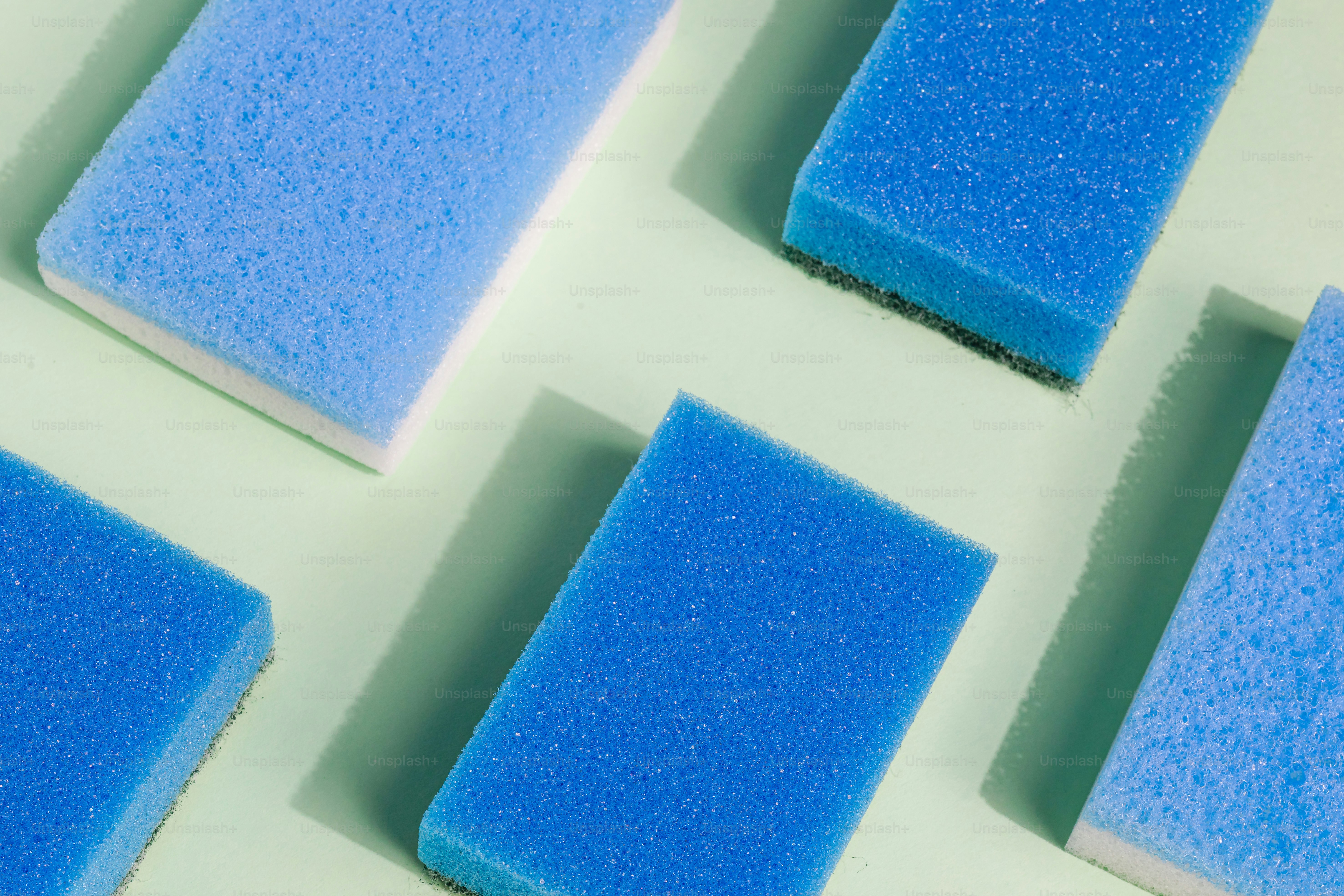 Several blue cleaning sponges on a light green surface.