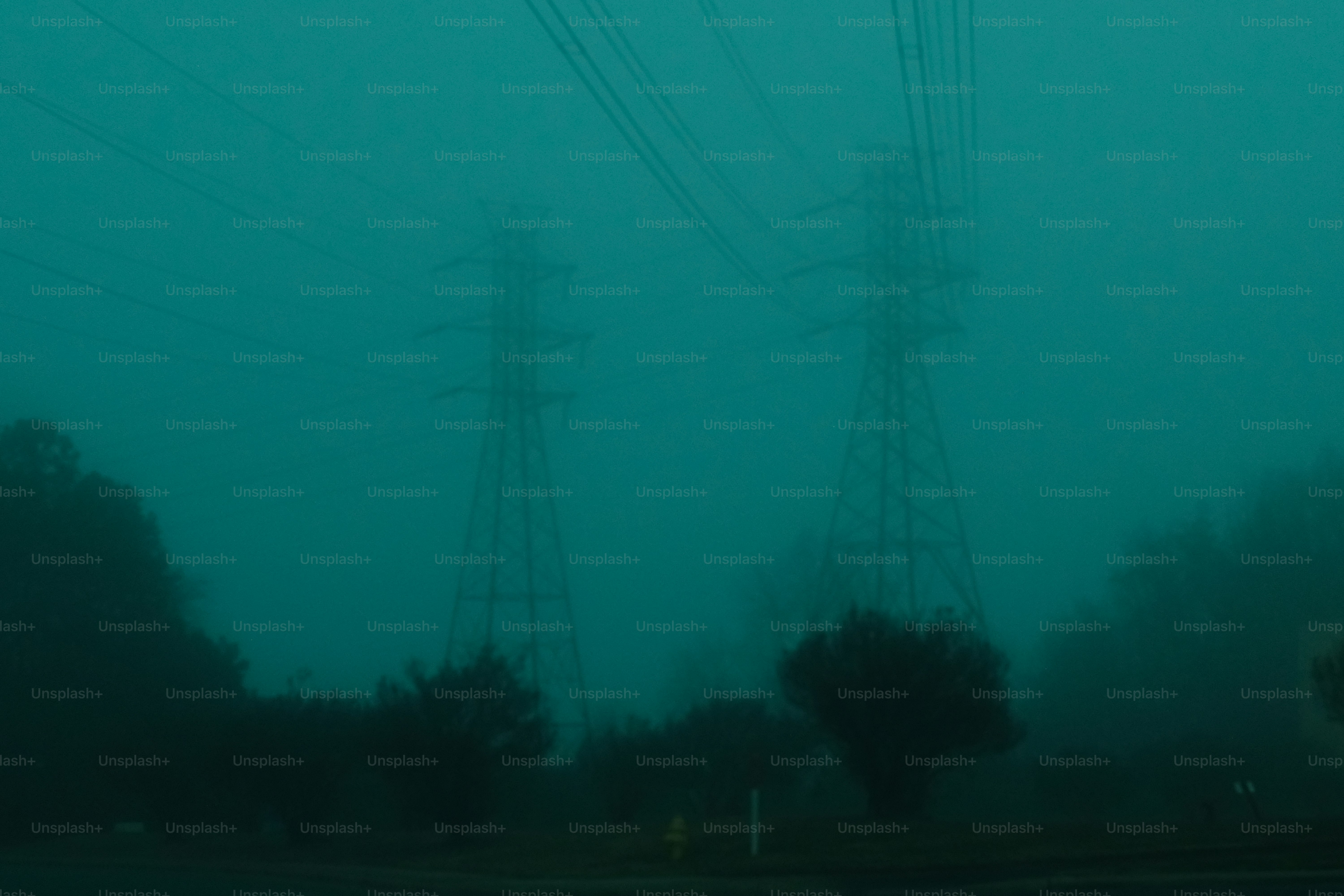 Two power line towers in a foggy teal landscape.