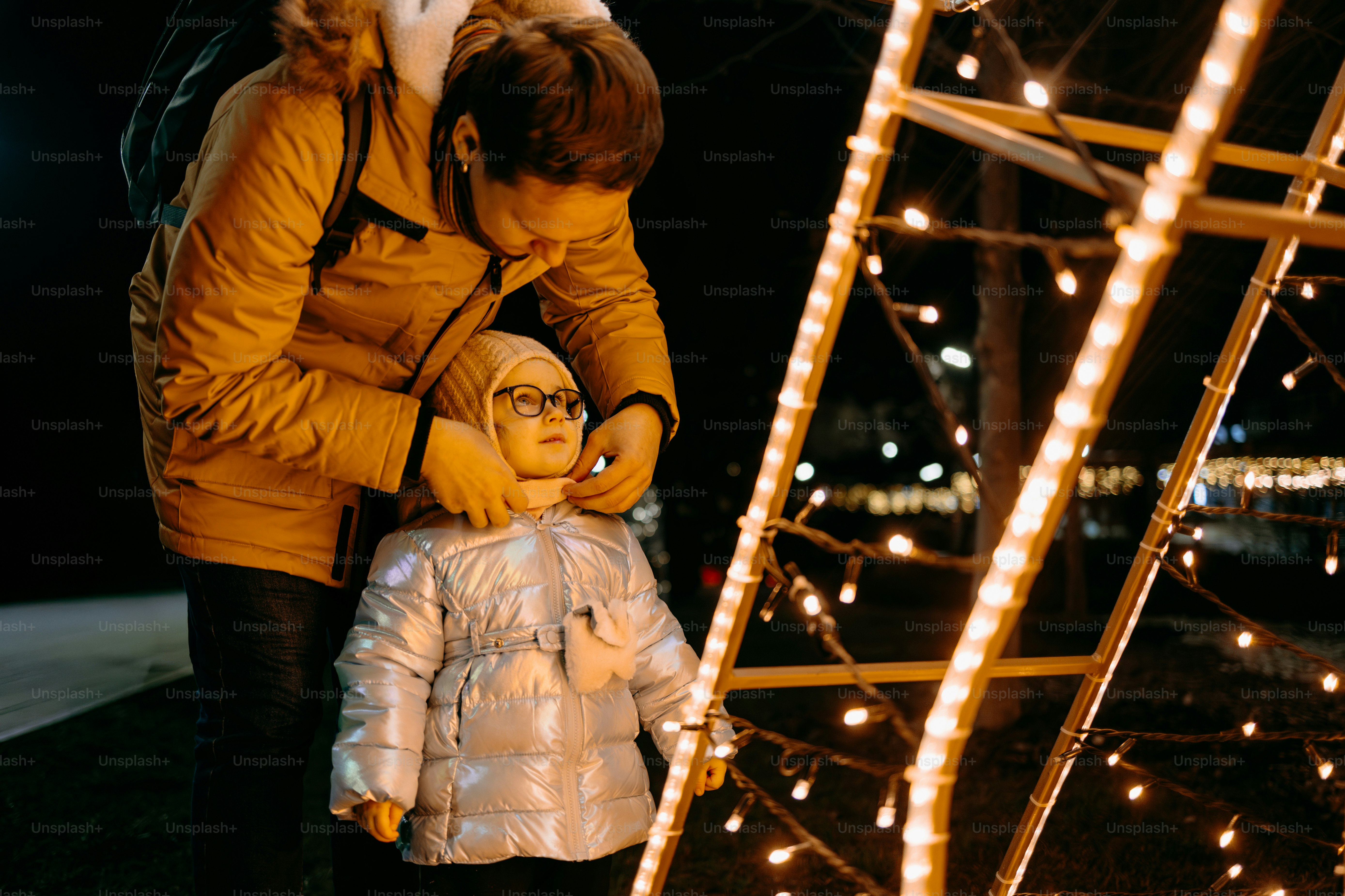 Adulto ajusta la bufanda del niño cerca de las luces de Navidad