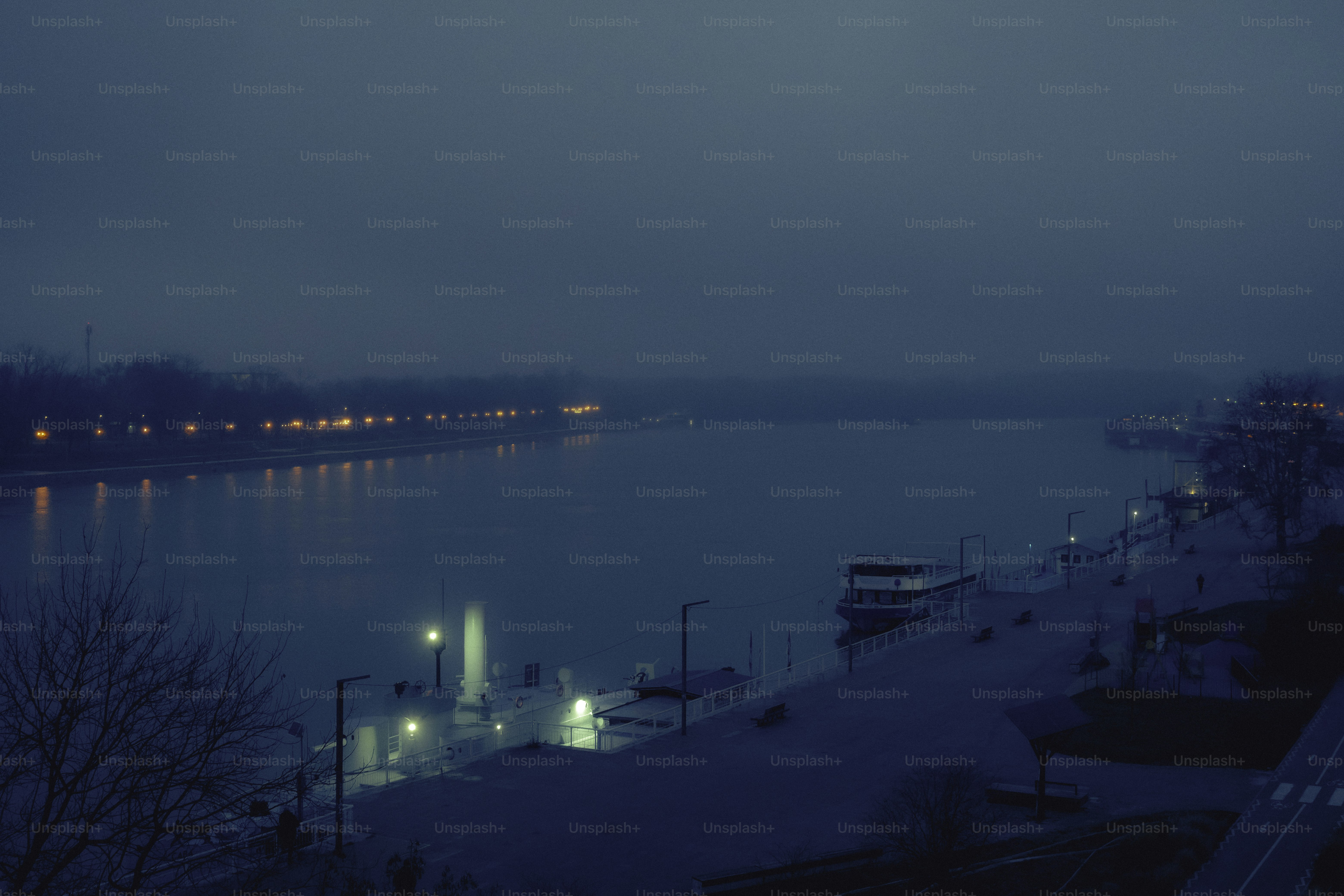 Nebliges Flussufer mit fernen Stadtlichtern bei Einbruch der Dämmerung