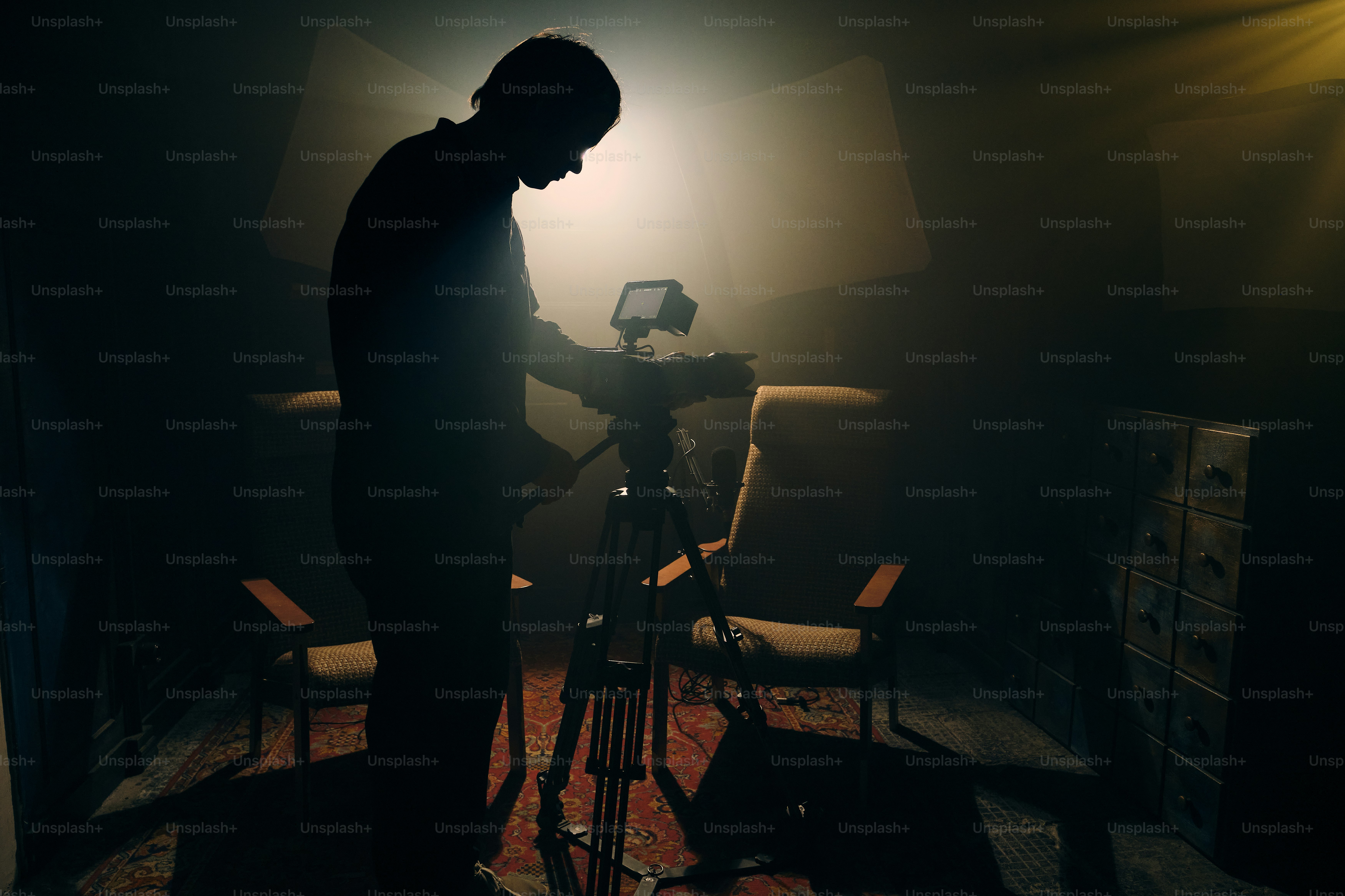 Filmmaker setting up camera on tripod in dimly lit room.