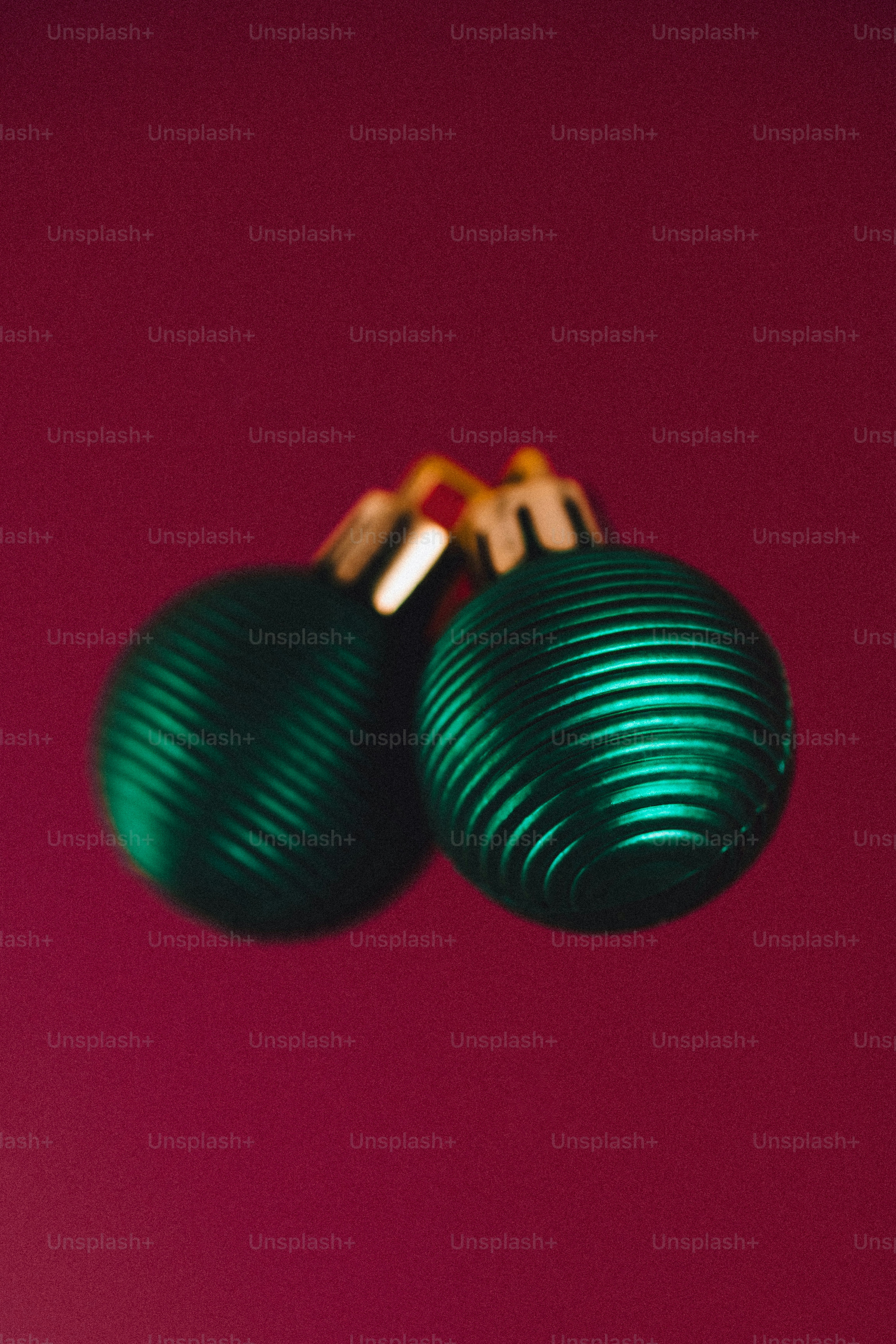 Two green christmas ornaments on a maroon background