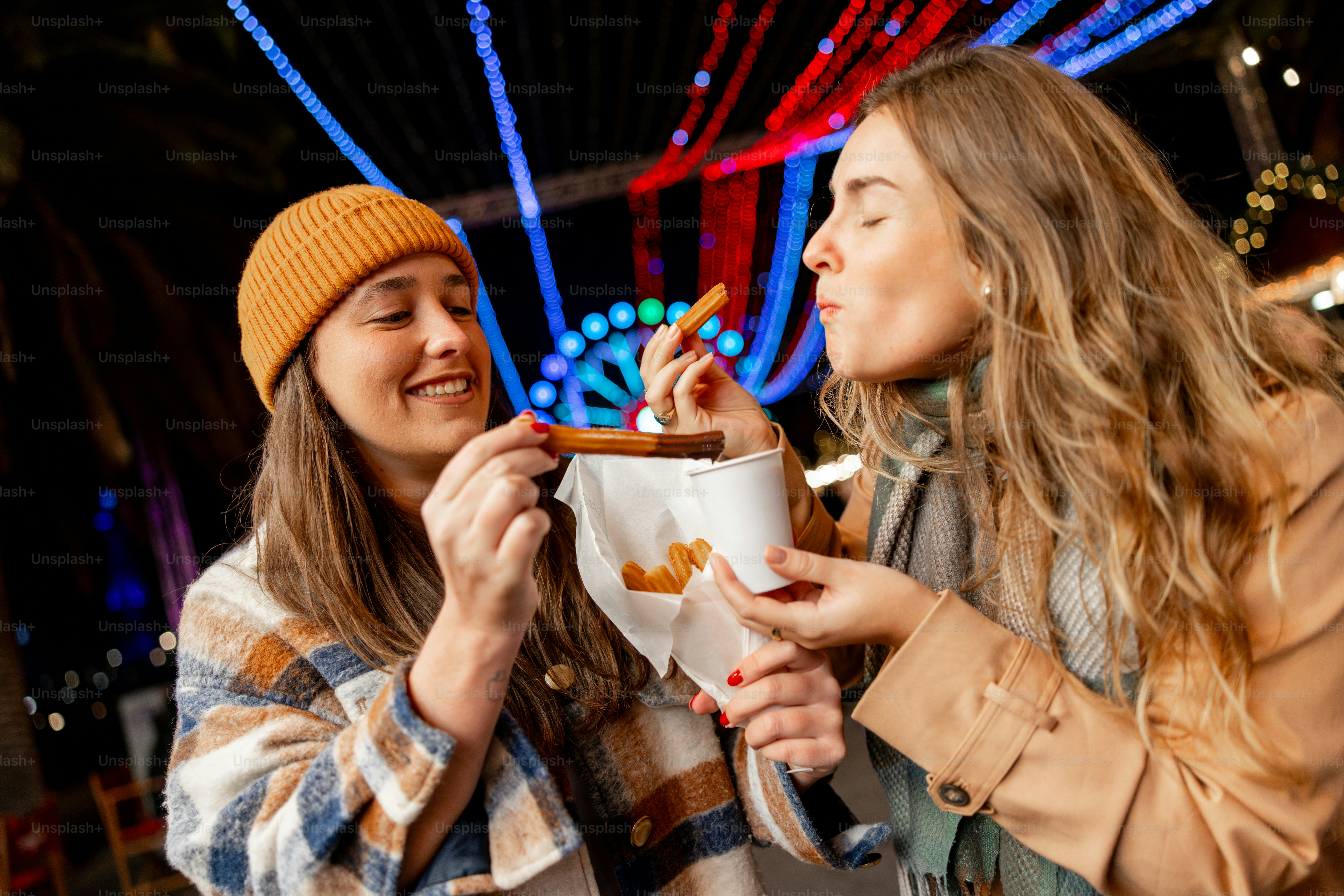 Two women enjoying fried food at a festive market.