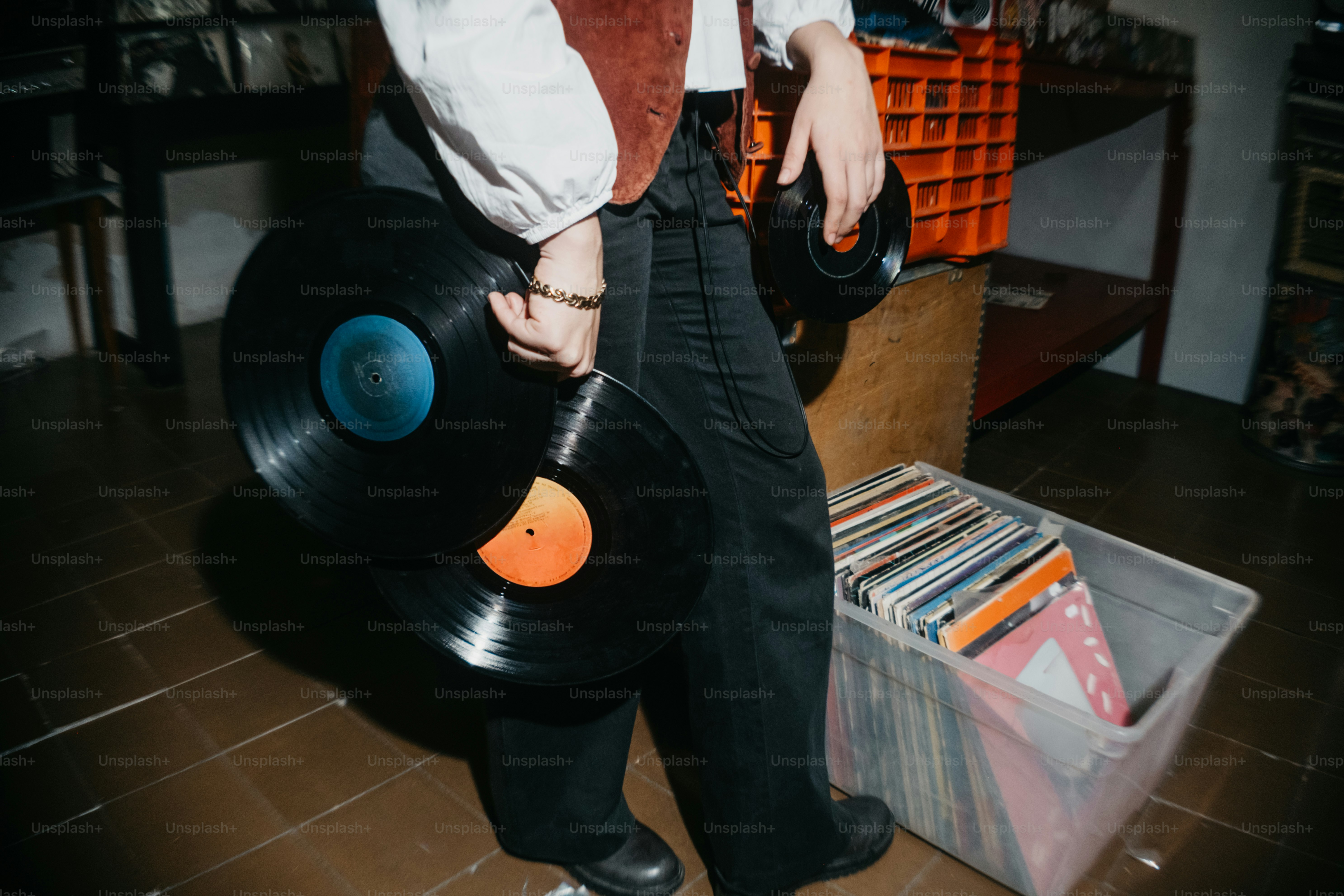 Person holding vinyl records near a crate of records