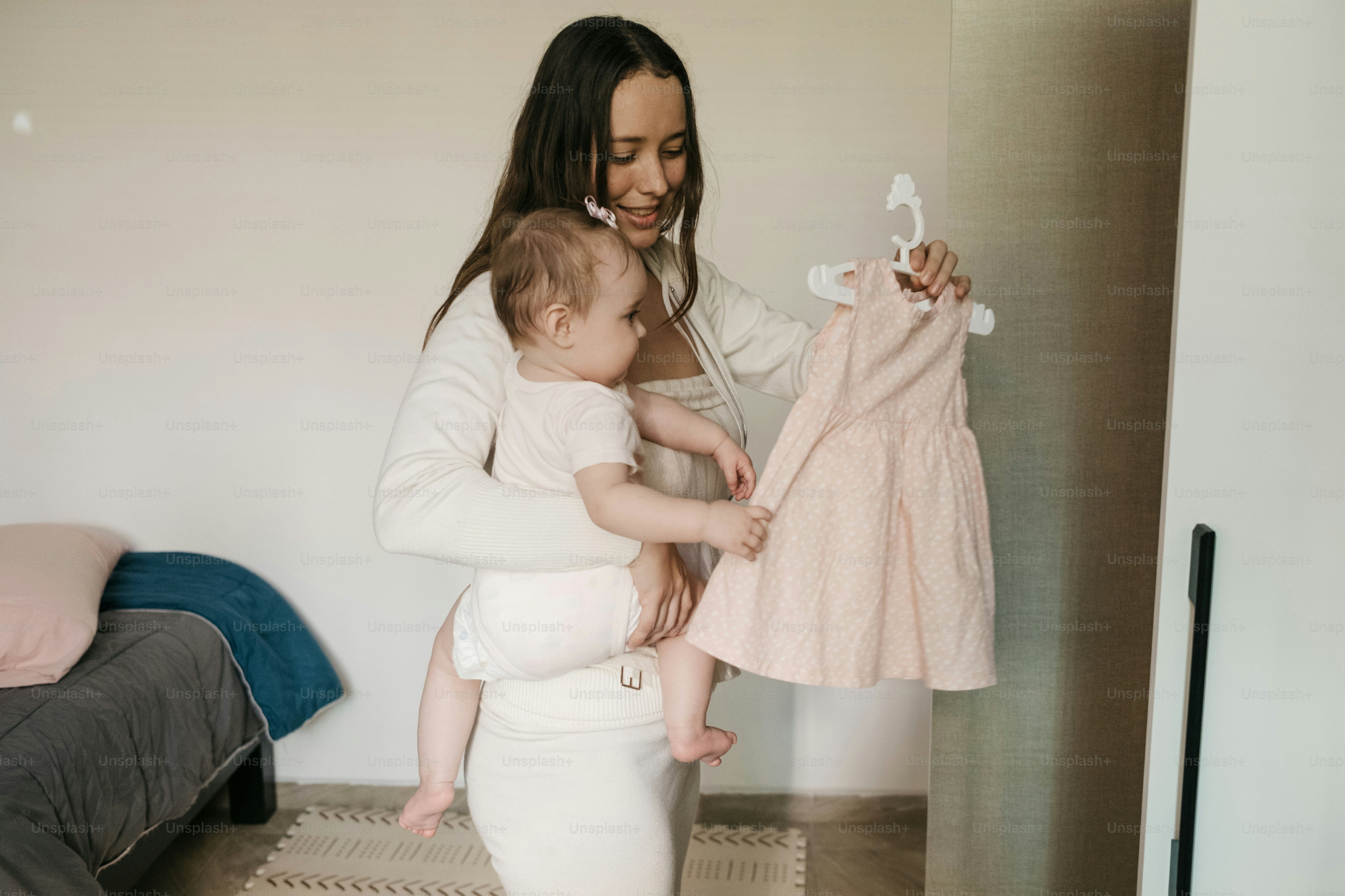 Die Mutter hält das Baby, während sie ein rosa Kleid auswählt.