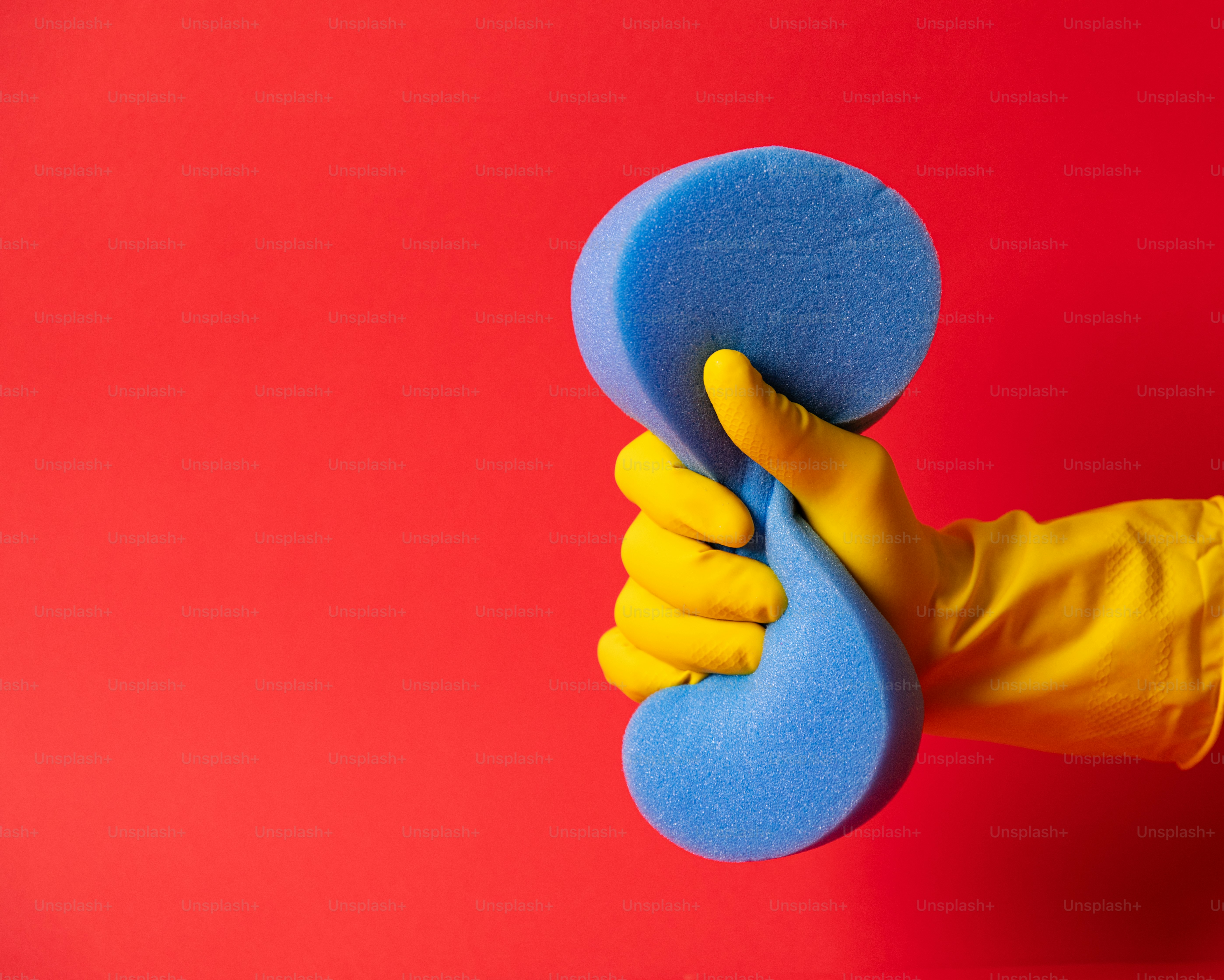 Main dans le gant jaune pressant l’éponge bleue