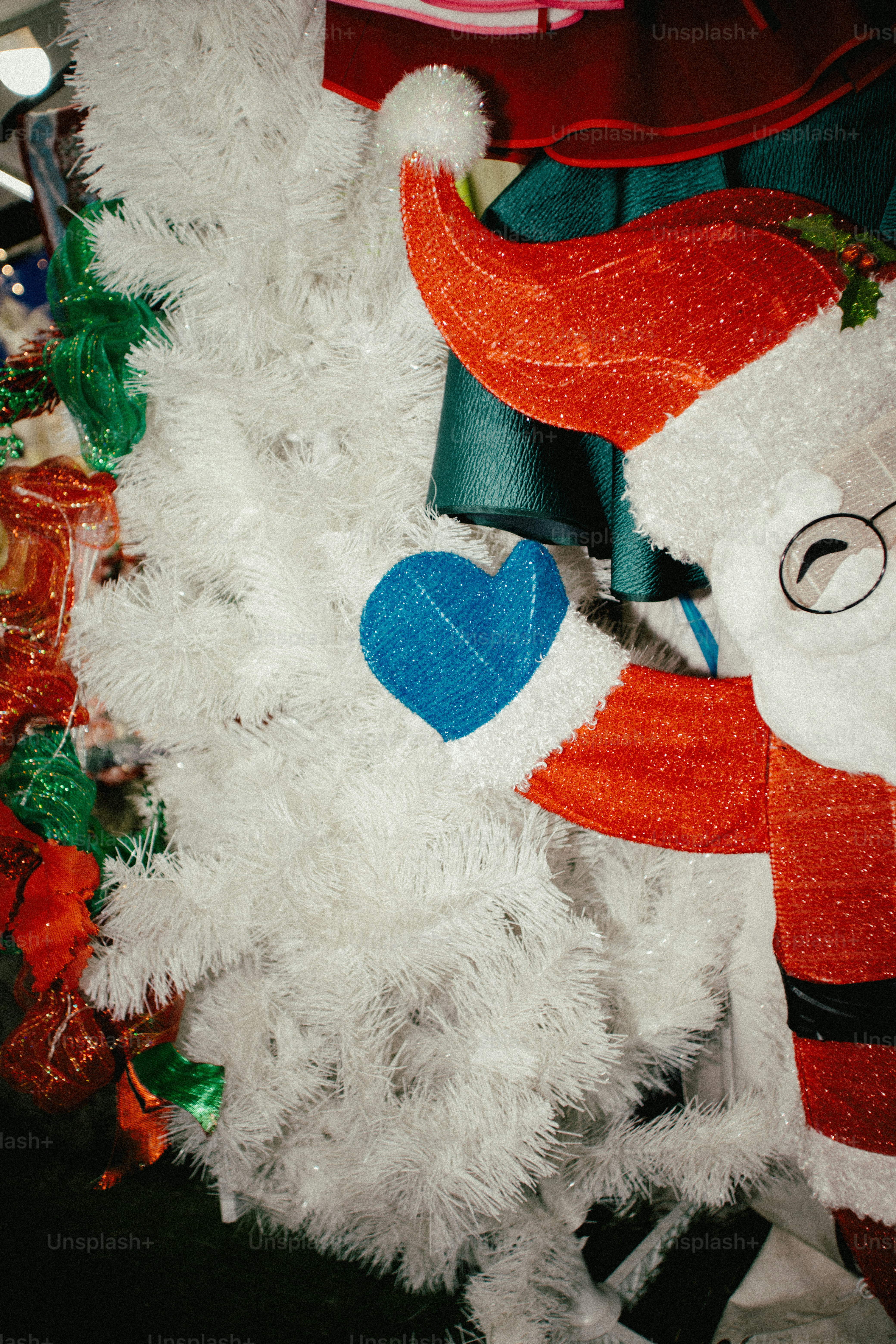 Santa holding a blue heart near a white christmas tree