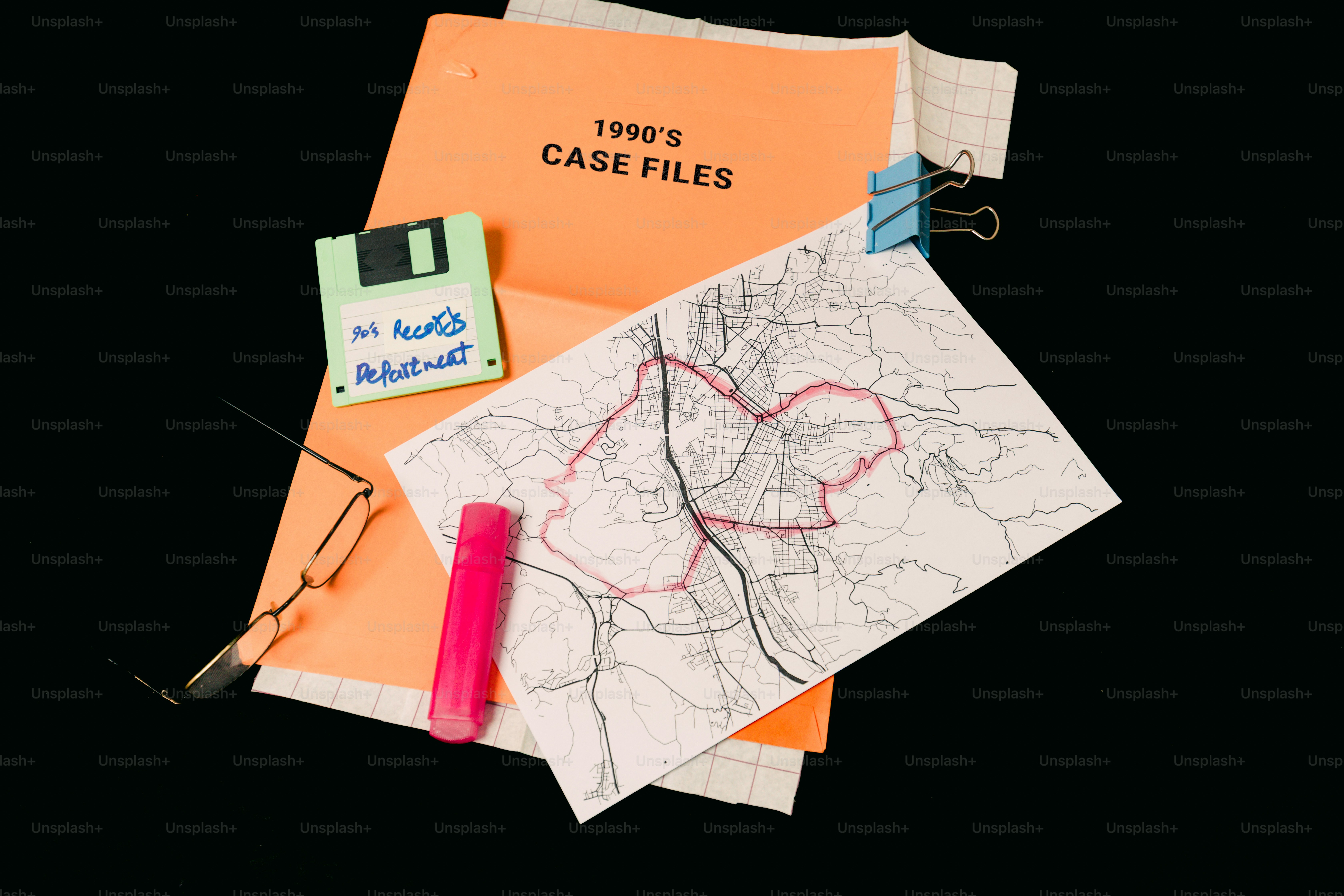 Case files, map, floppy disk, and glasses on black