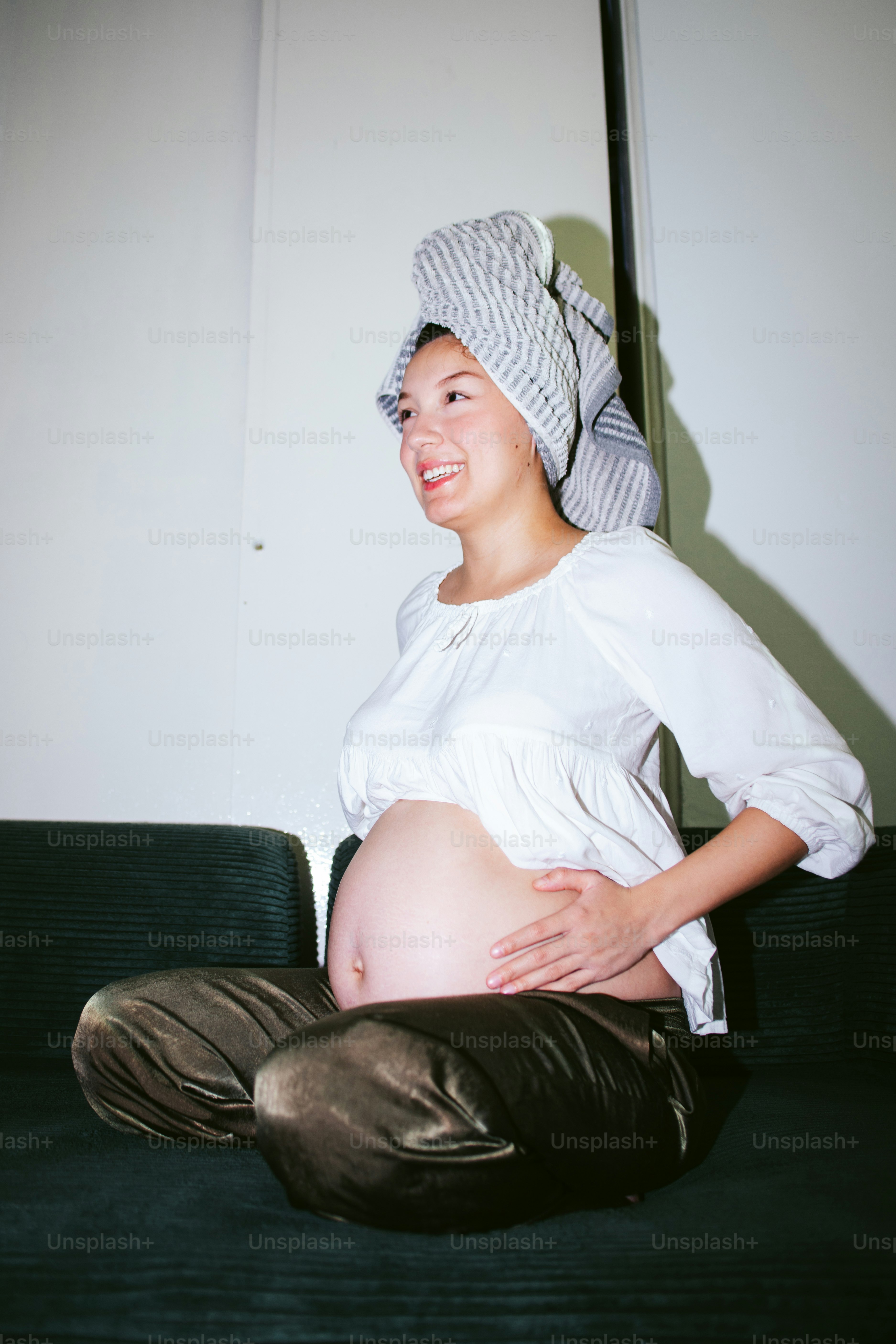 Pregnant woman with towel on head sits on couch.
