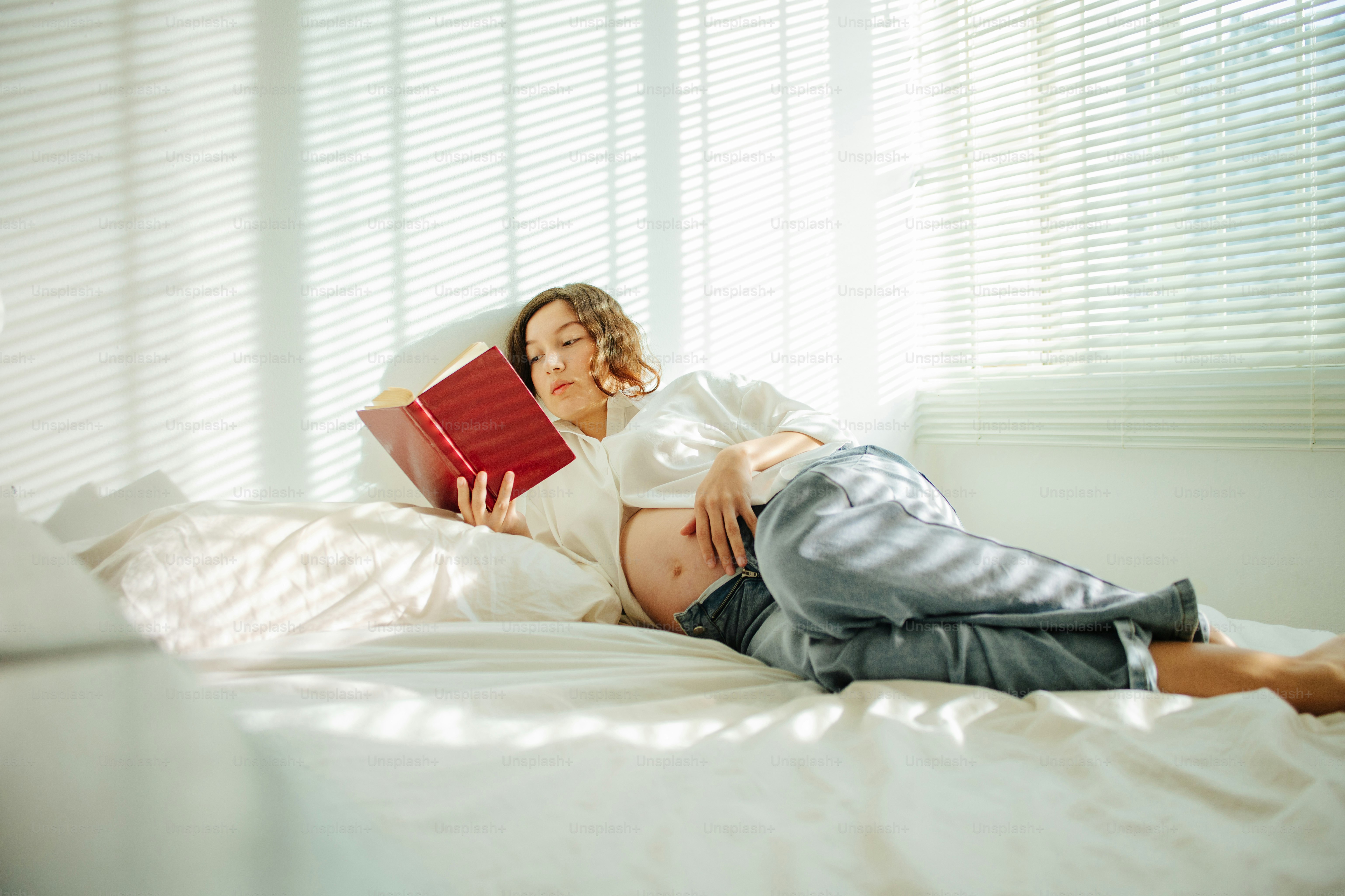 Pregnant woman resting and reading a book in bed.