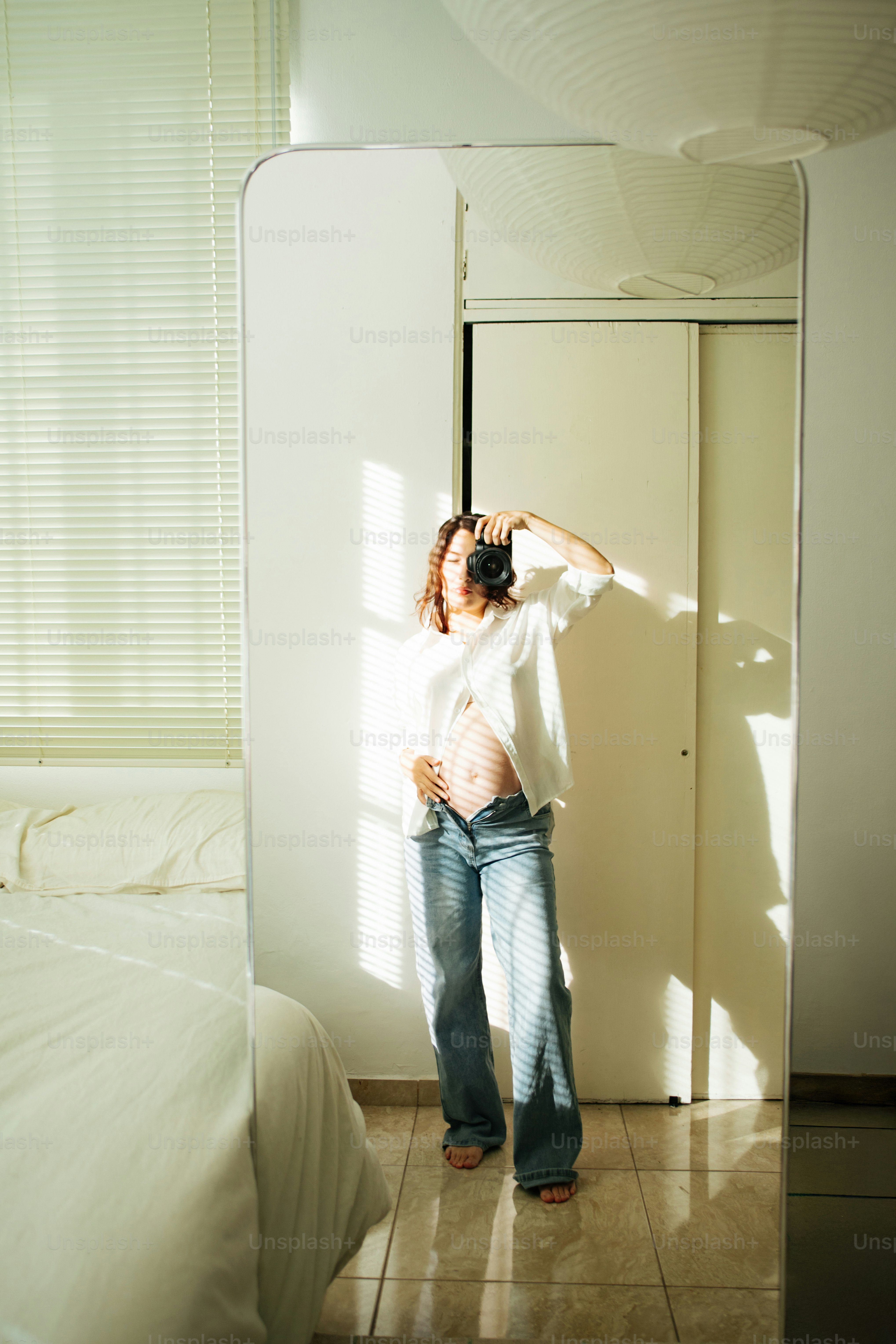 Pregnant woman taking a mirror selfie with a camera.