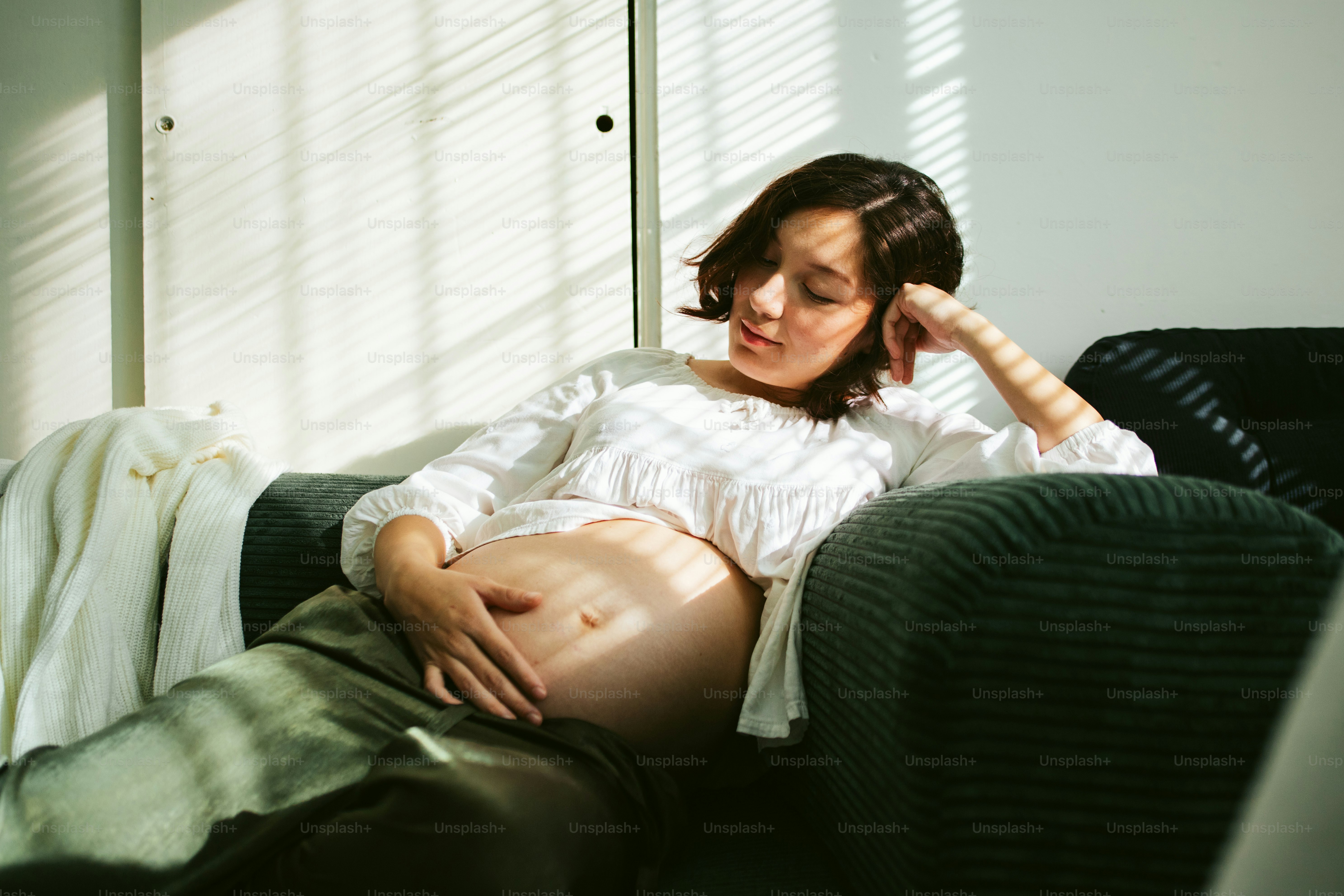 Pregnant woman resting on a sofa in sunlight.