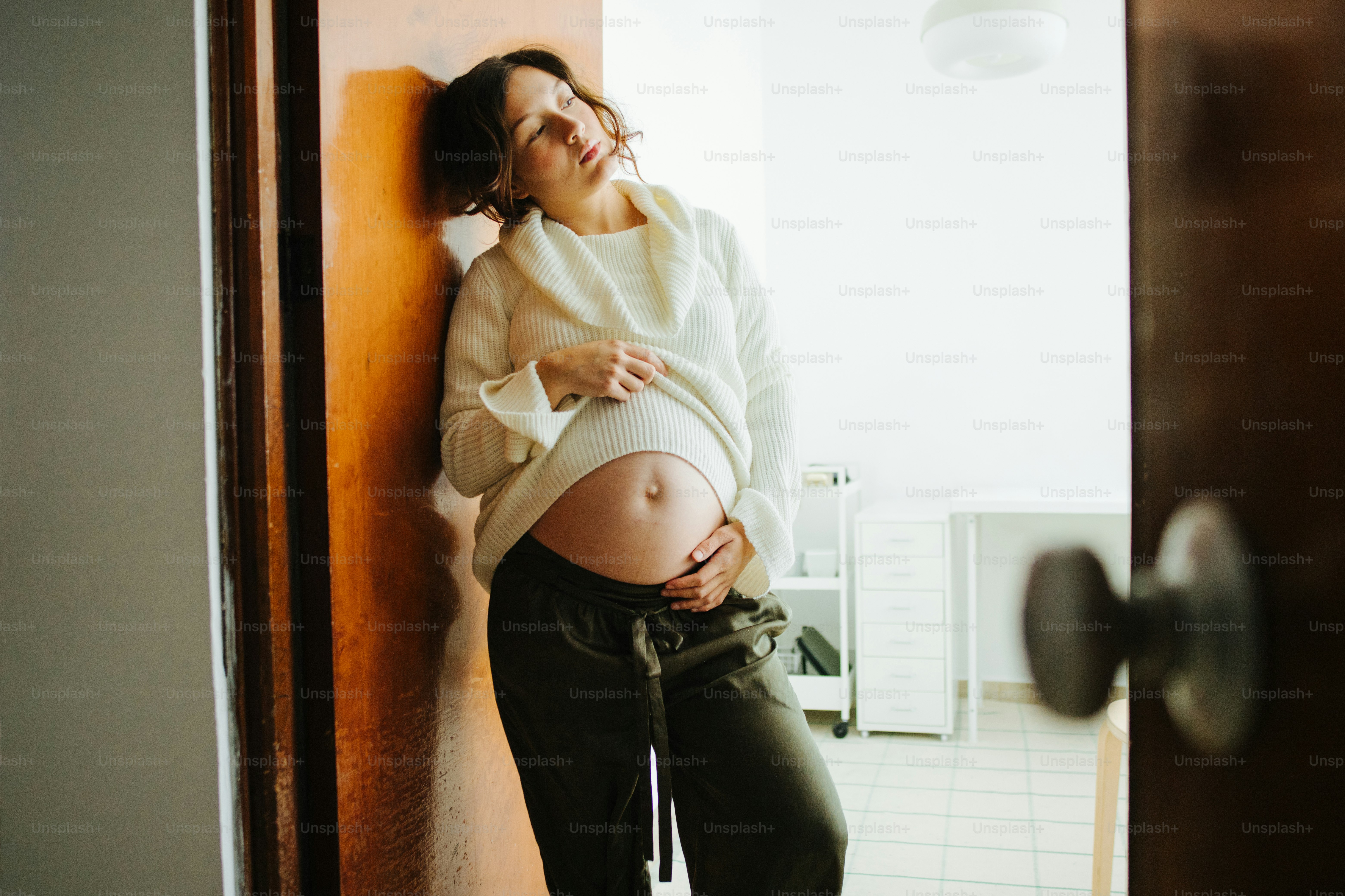 Pregnant woman leaning against wall, holding belly.