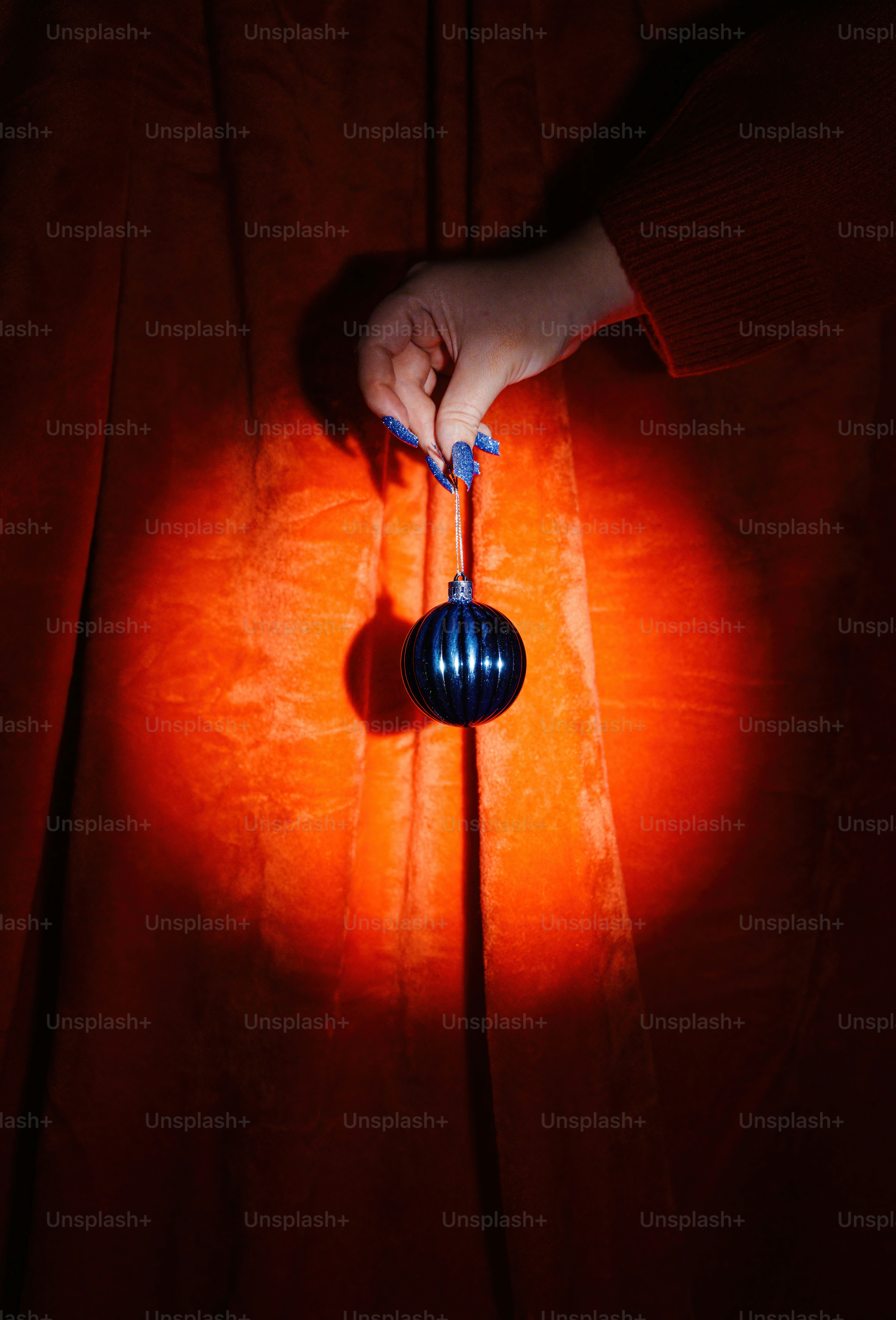 Hand holding a dark blue christmas ornament against red velvet.