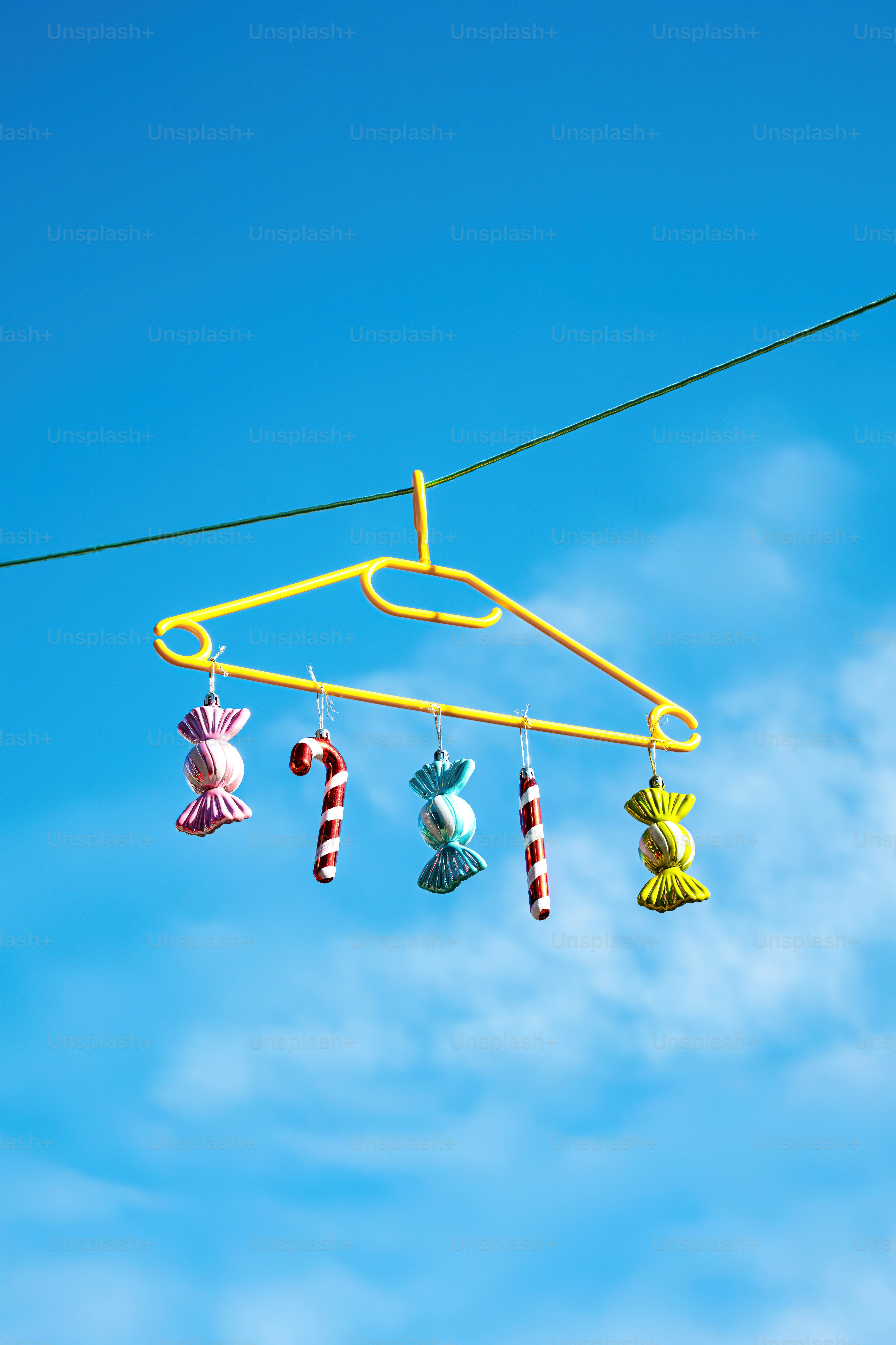 Candy ornaments hanging from a yellow hanger against blue sky