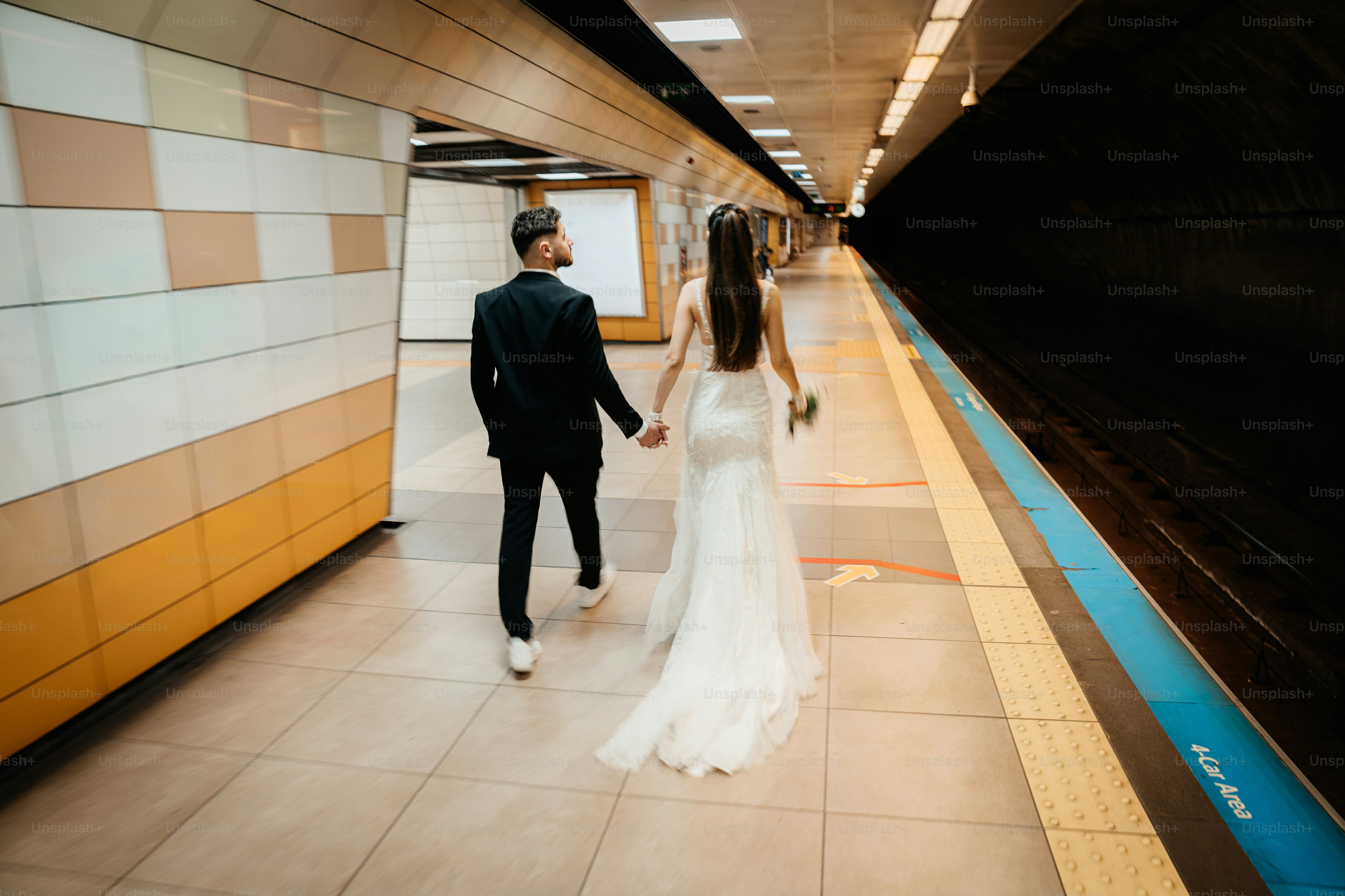 Couple in wedding attire walks down subway platform.