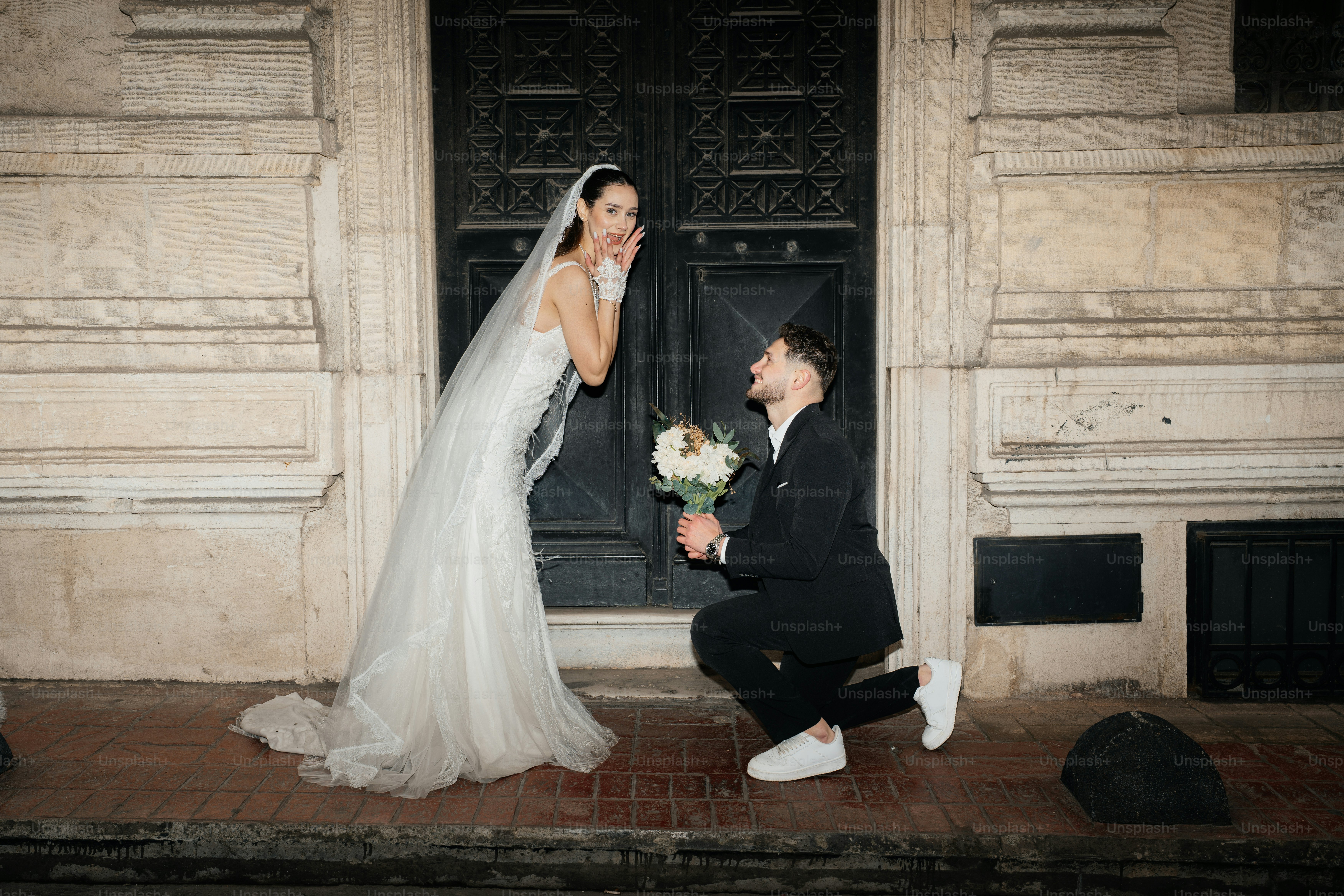 Groom proposes to bride with flowers outside building