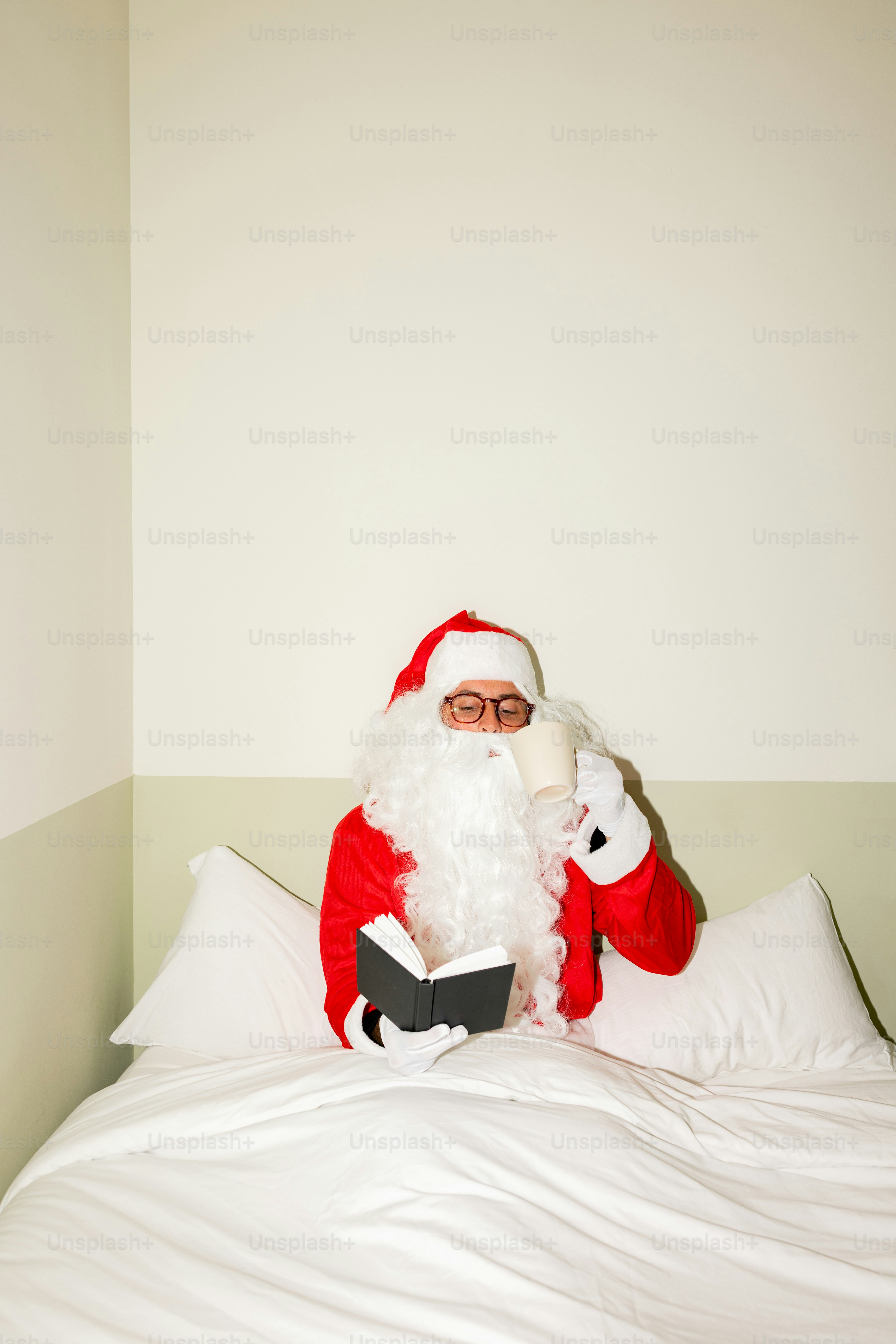 Santa claus reading a book in bed with a drink.