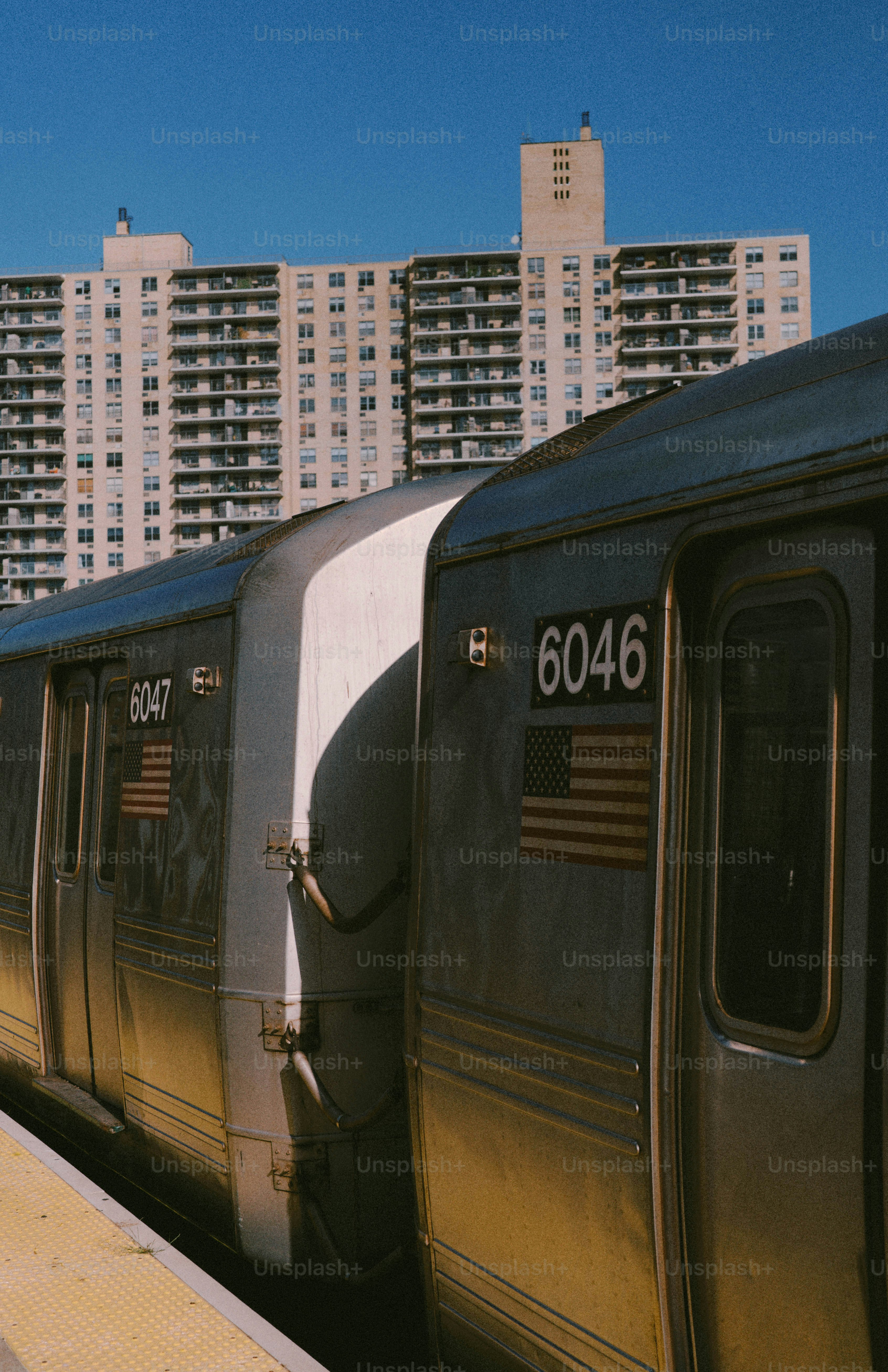 Subway train cars parked at a station with apartment buildings.