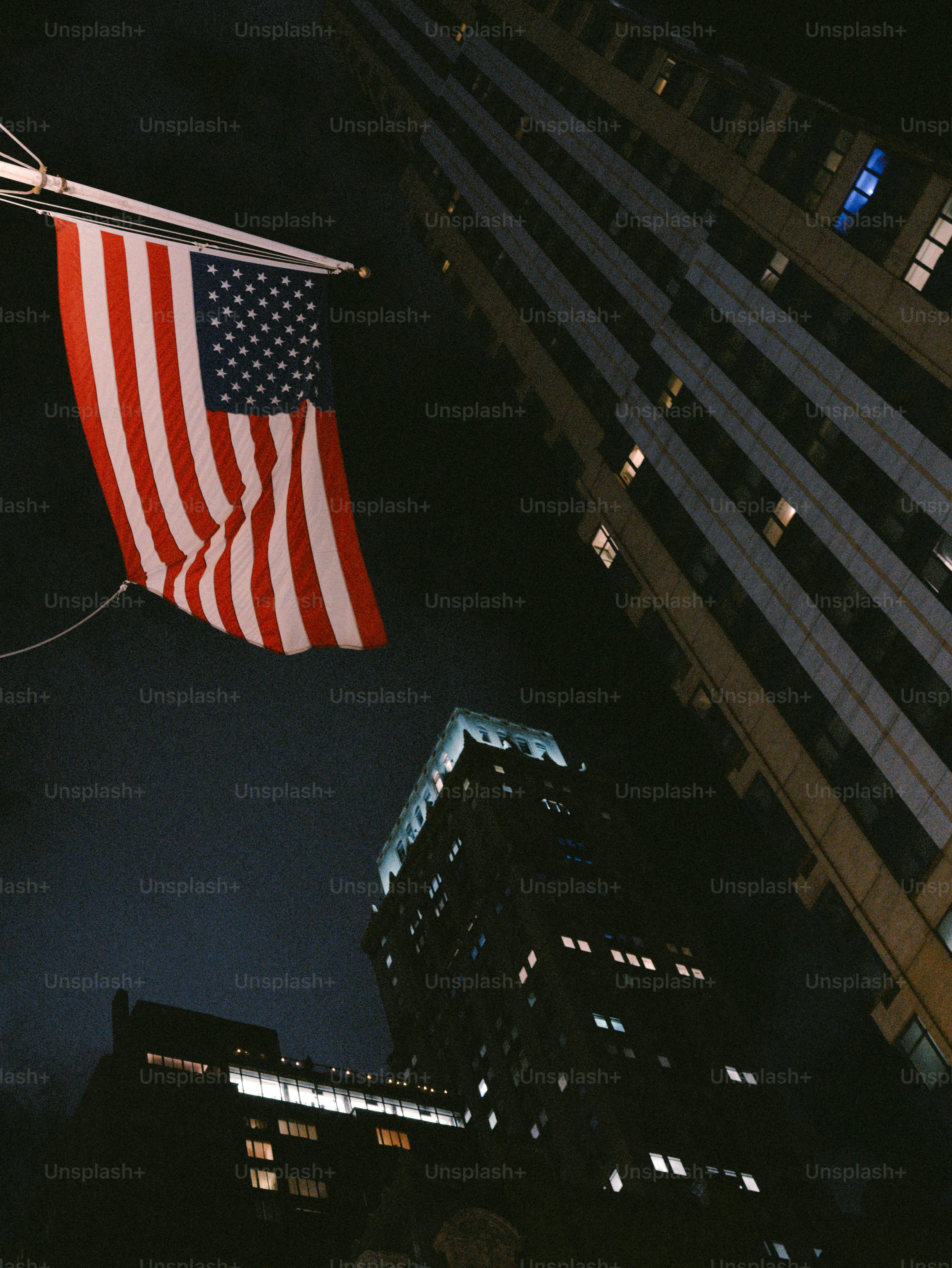 American flag flies near illuminated city buildings at night