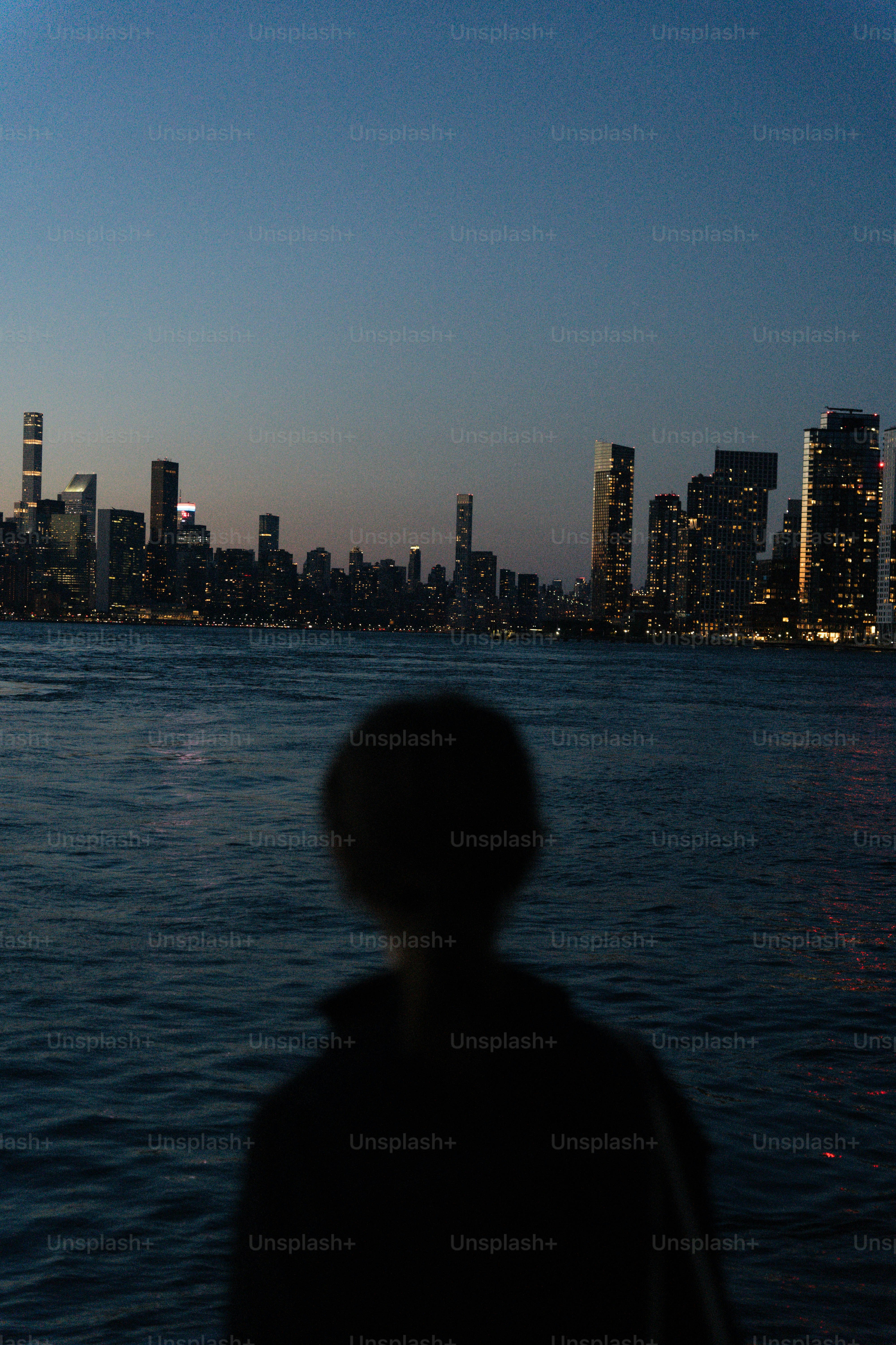 水面越しに街の灯りを見つめる人のシルエット。