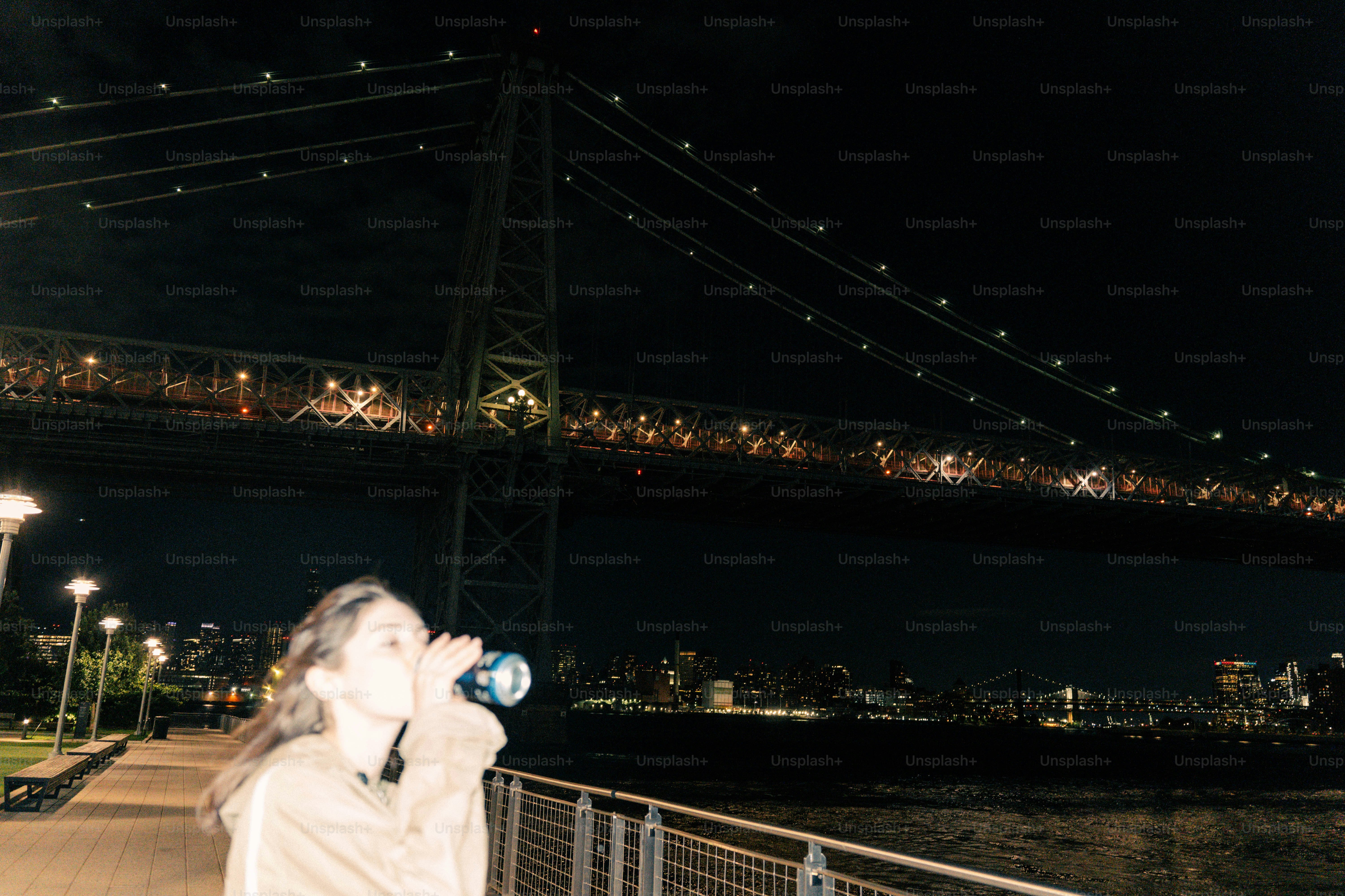 Woman drinking from bottle near bridge at night