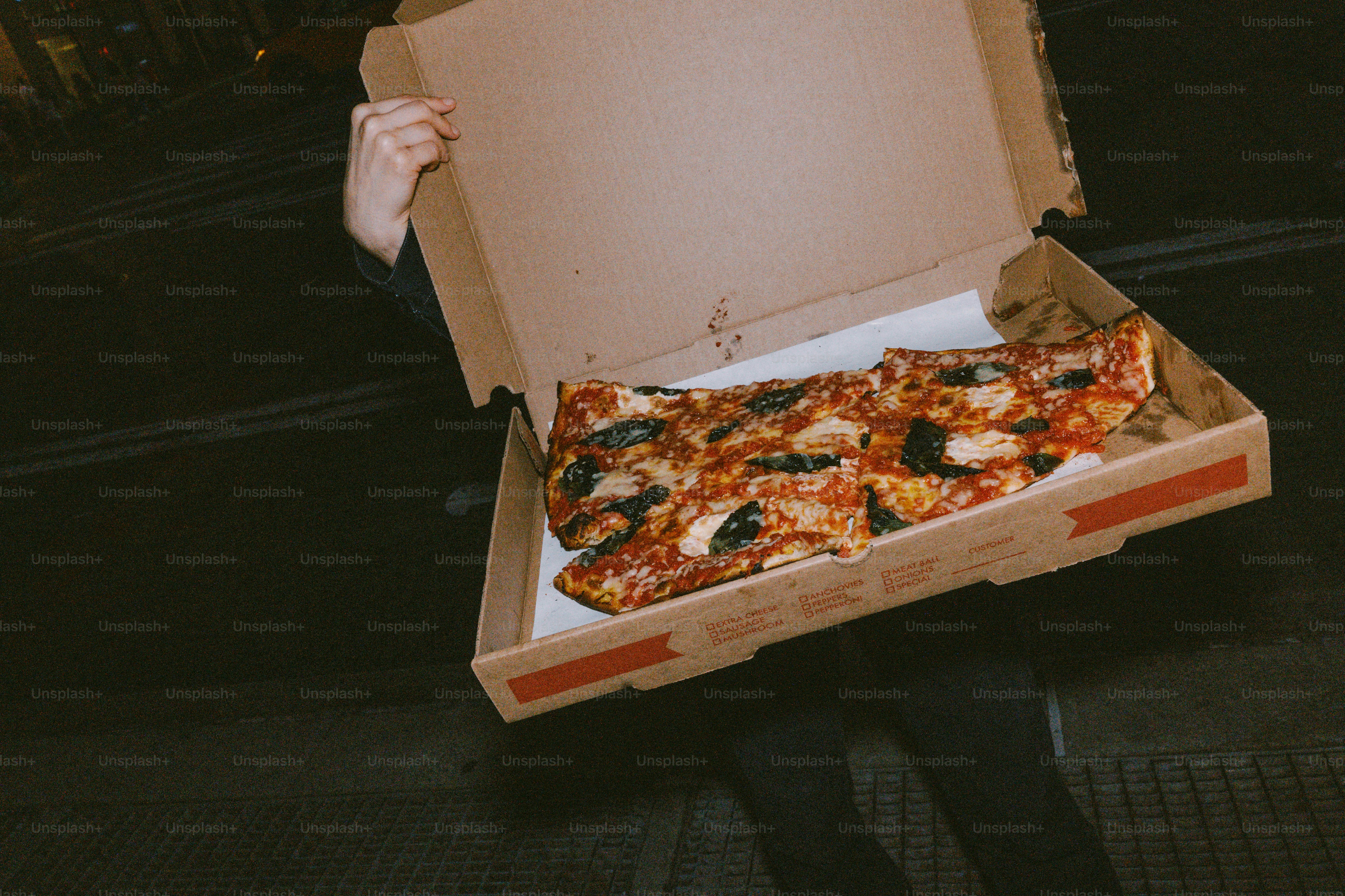 A person holds an open pizza box with slices inside.