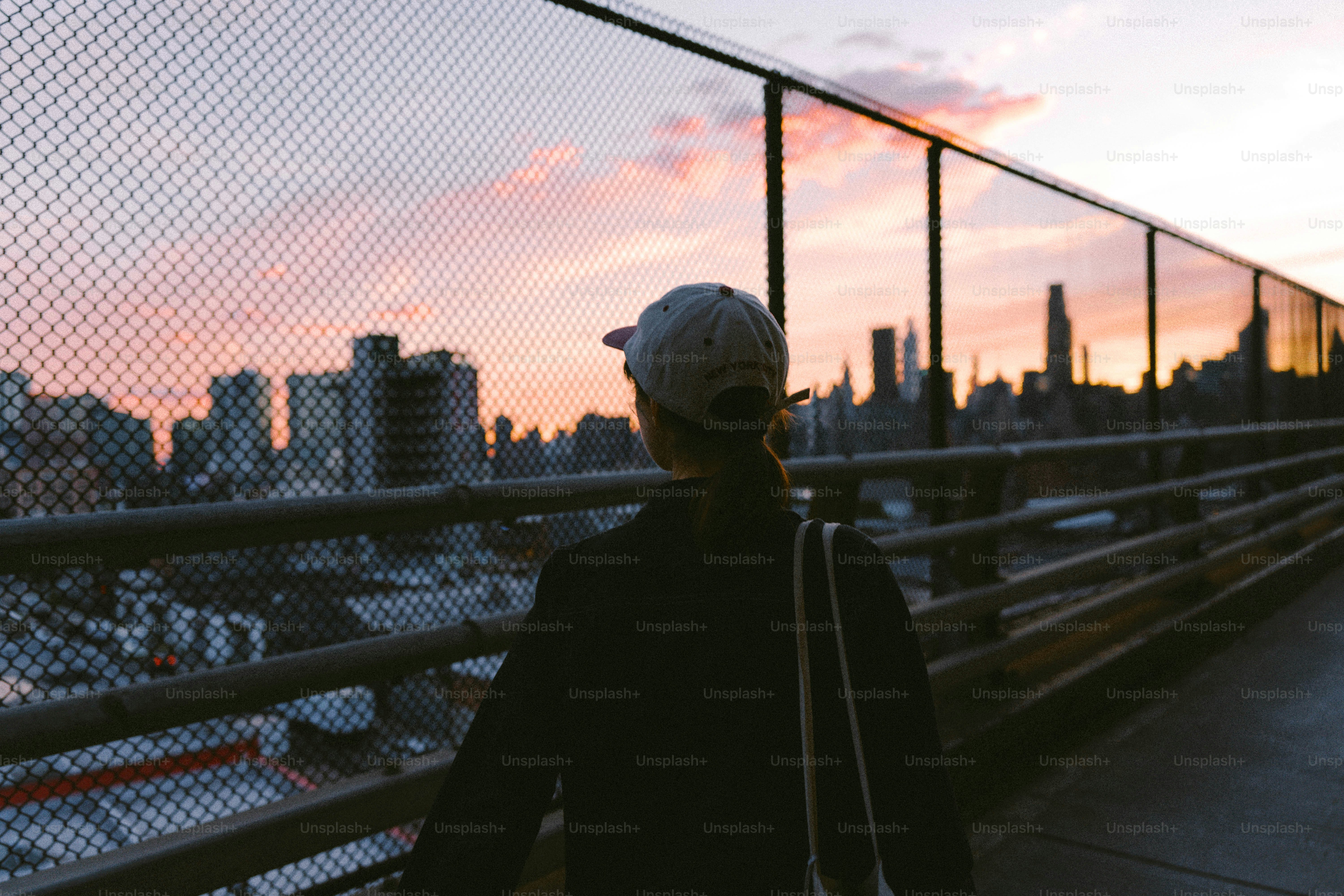 Person walking on a bridge towards city skyline at sunset