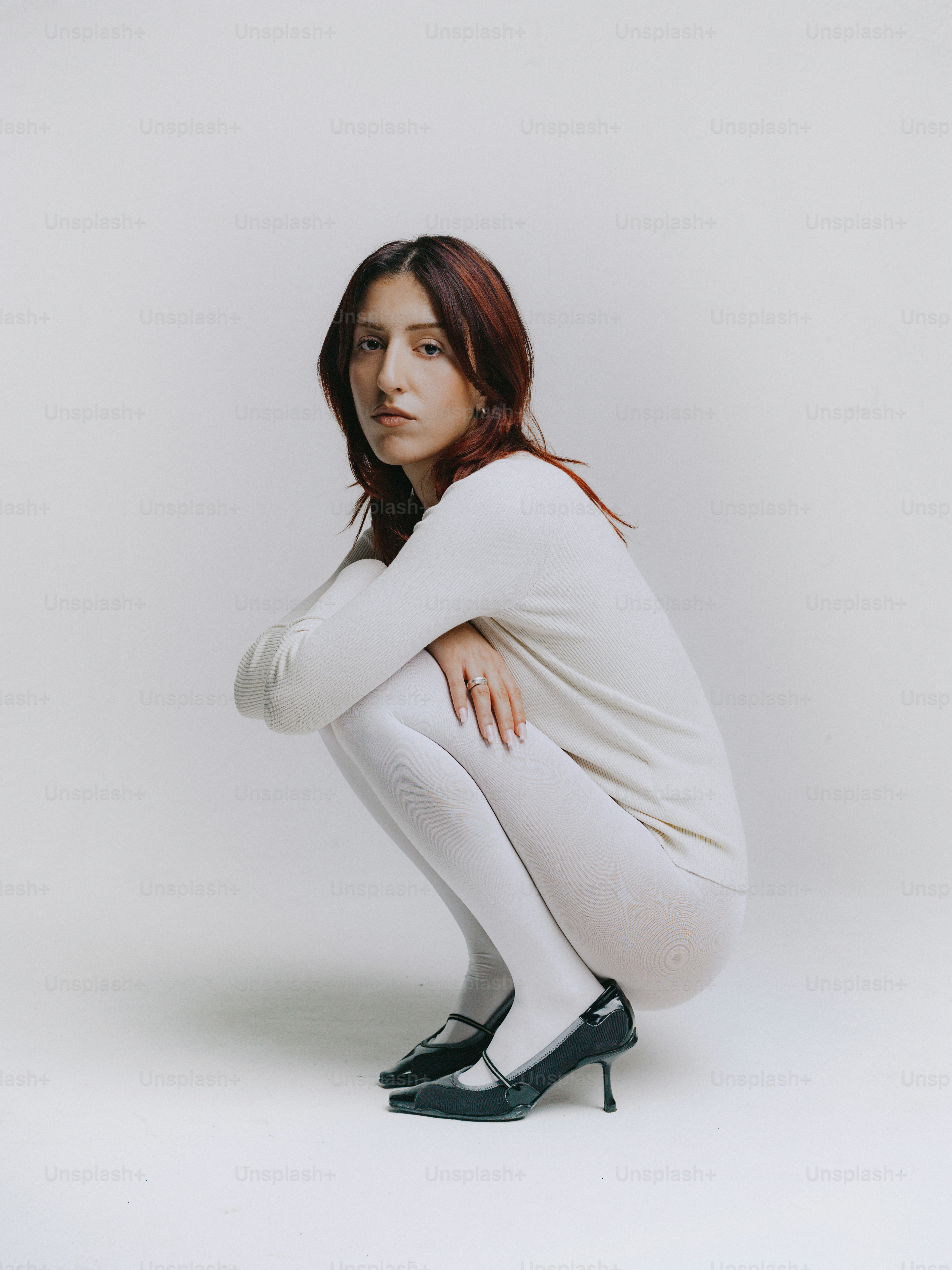 Donna in abito bianco accovacciata su sfondo bianco
