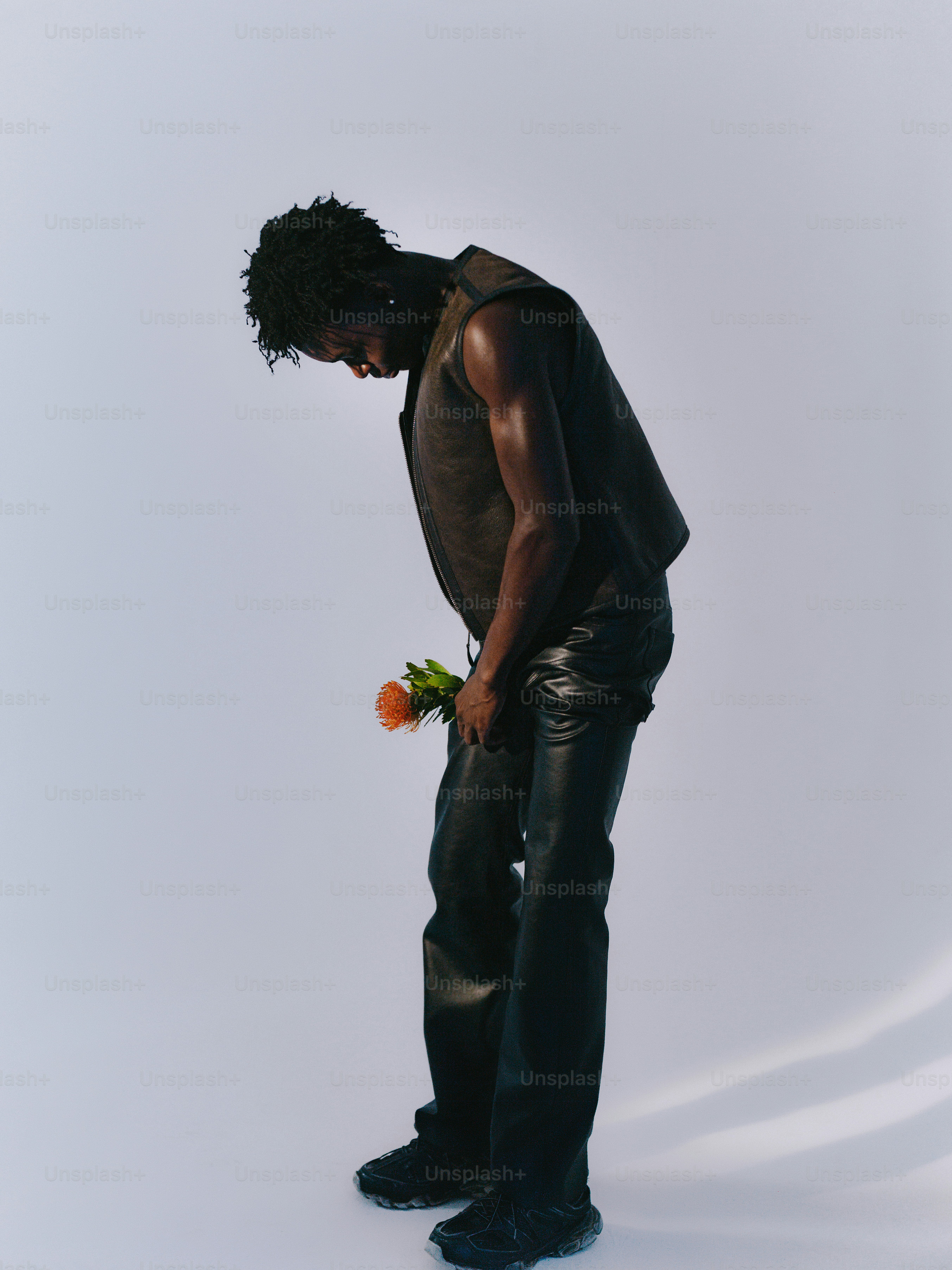 Un uomo con pantaloni di pelle tiene in mano un fiore arancione.