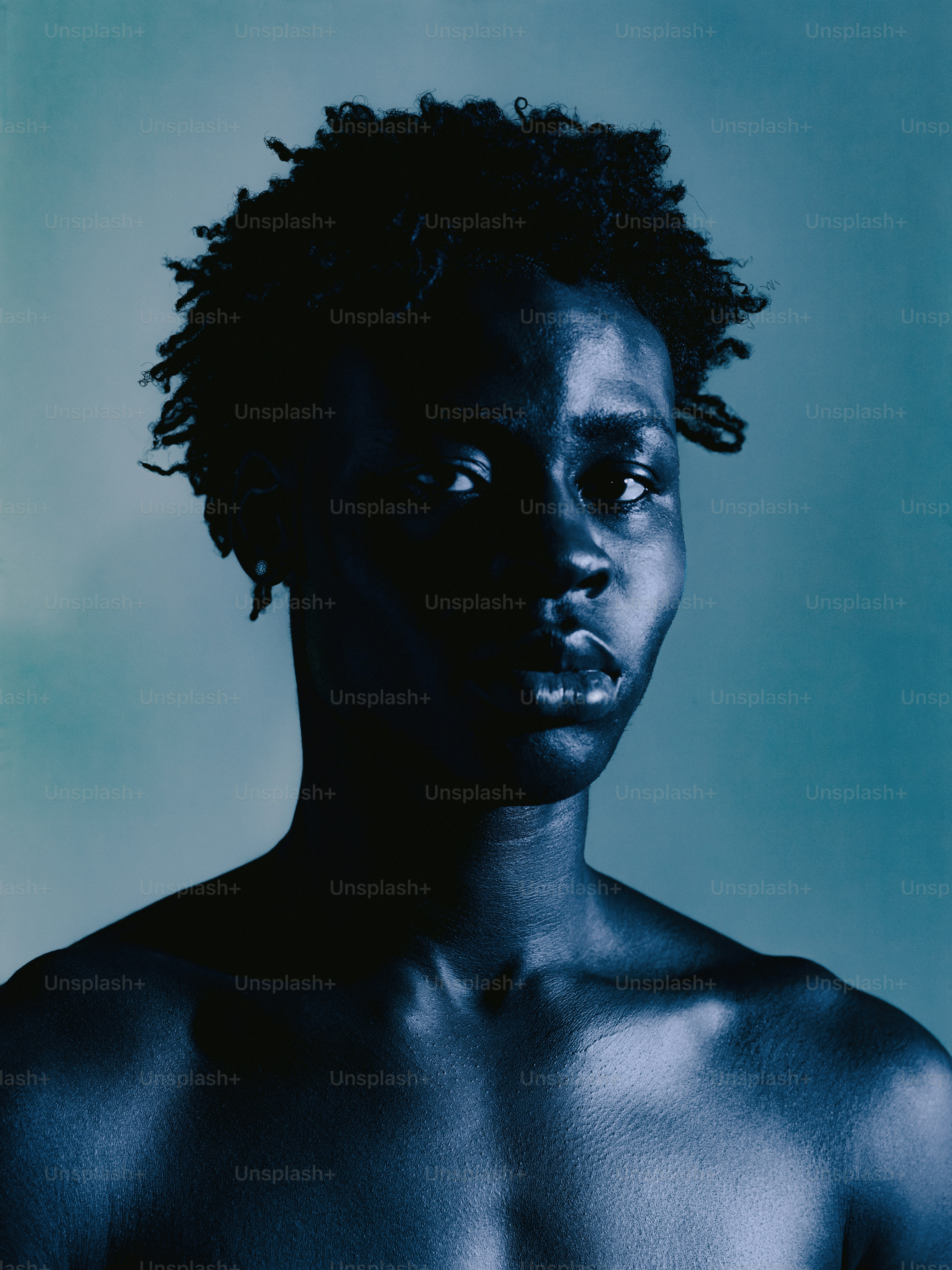 A dark-skinned person with curly hair against a blue background.