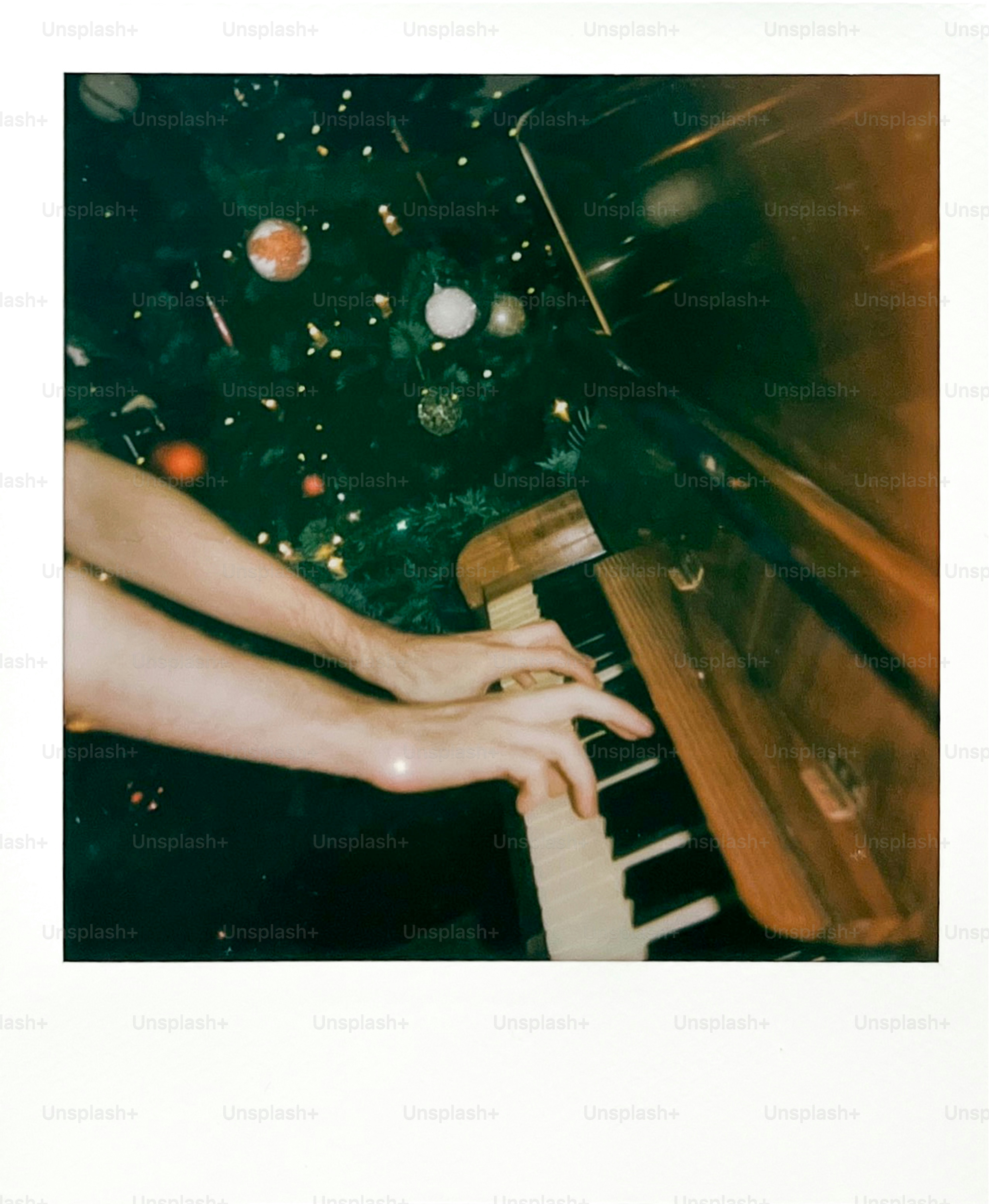 Hands playing piano next to a decorated christmas tree