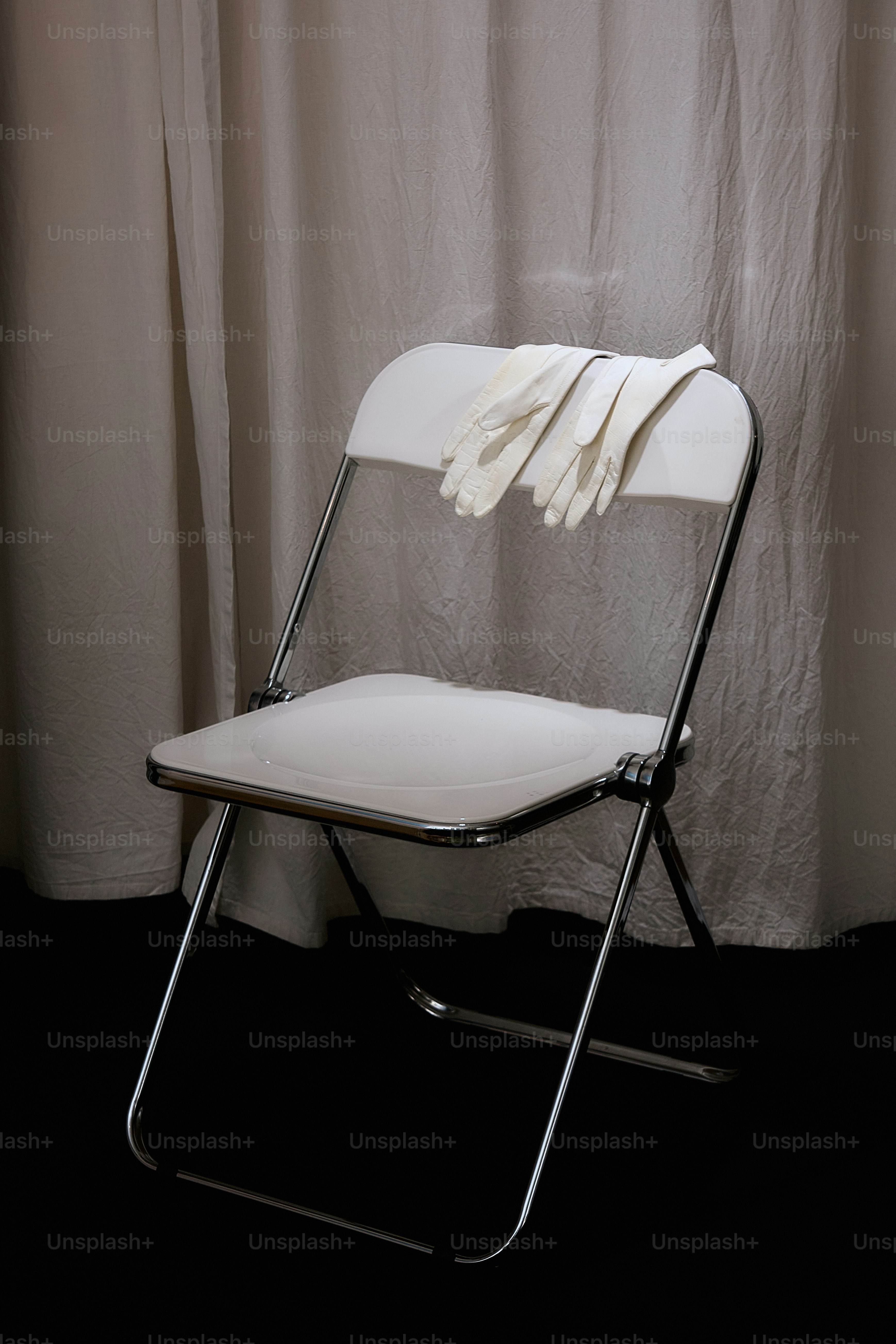 White folding chair with gloves on seat.