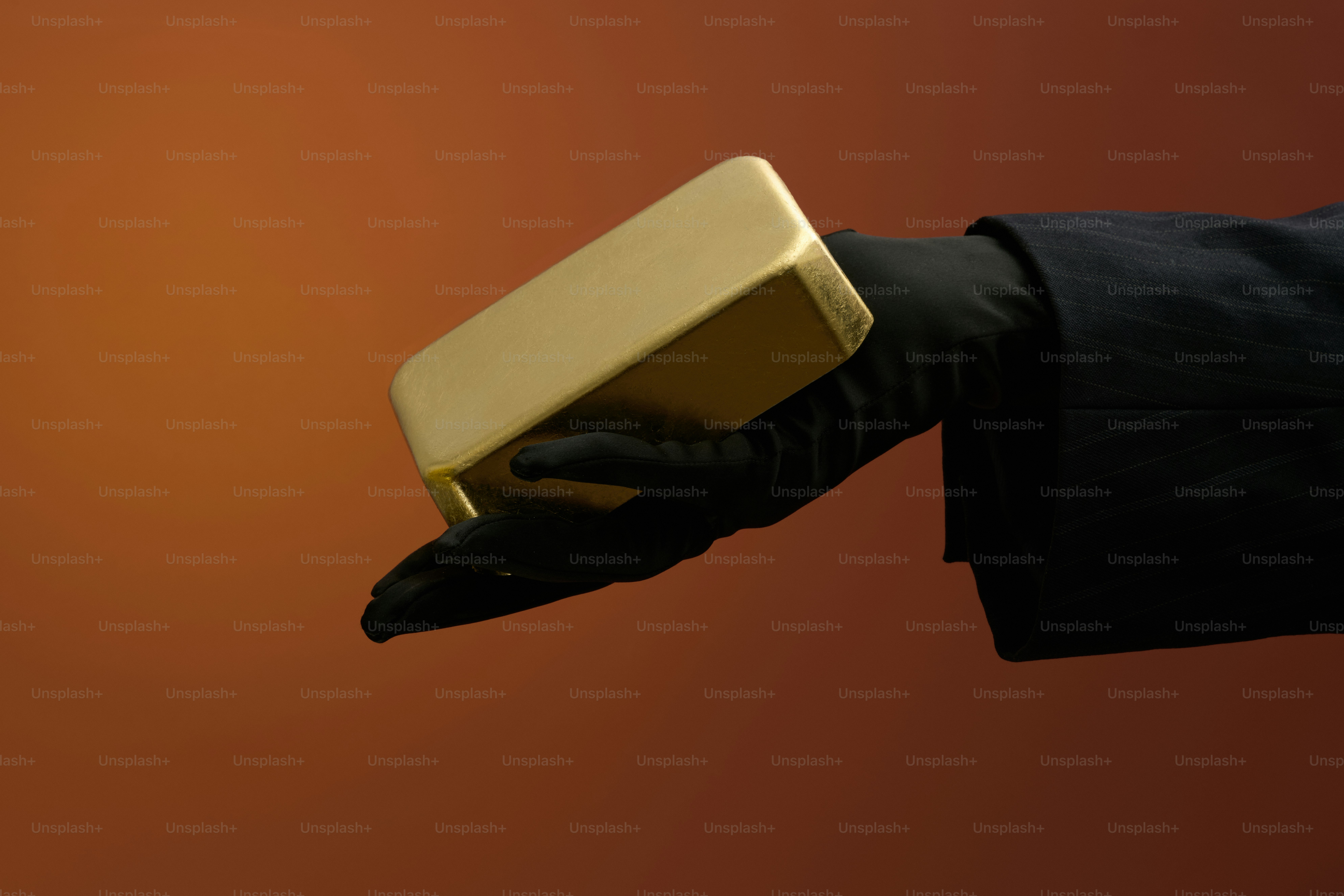 Hand in black glove holding a gold bar.