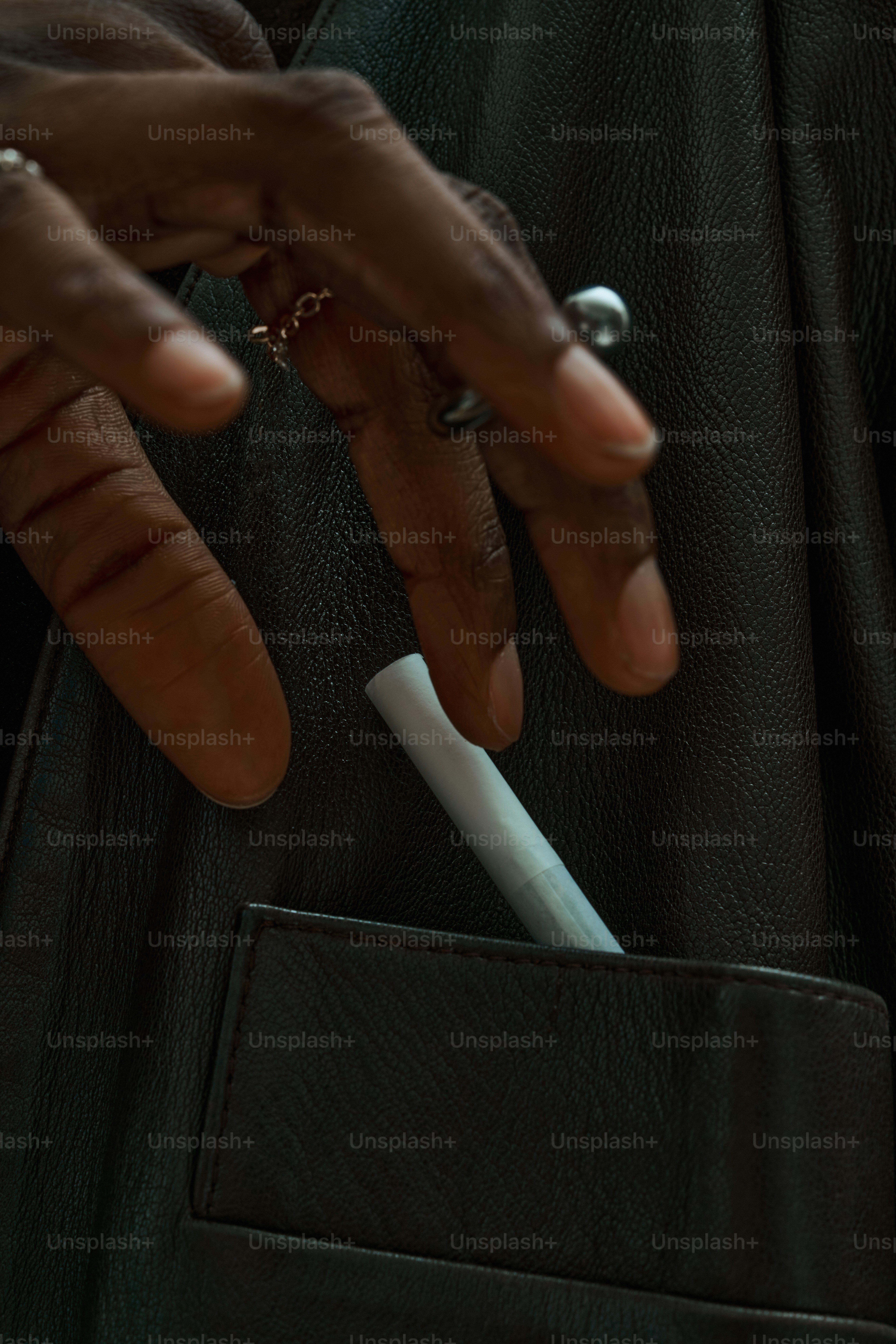 Dedos metiendo un cigarrillo en el bolsillo de una chaqueta de cuero