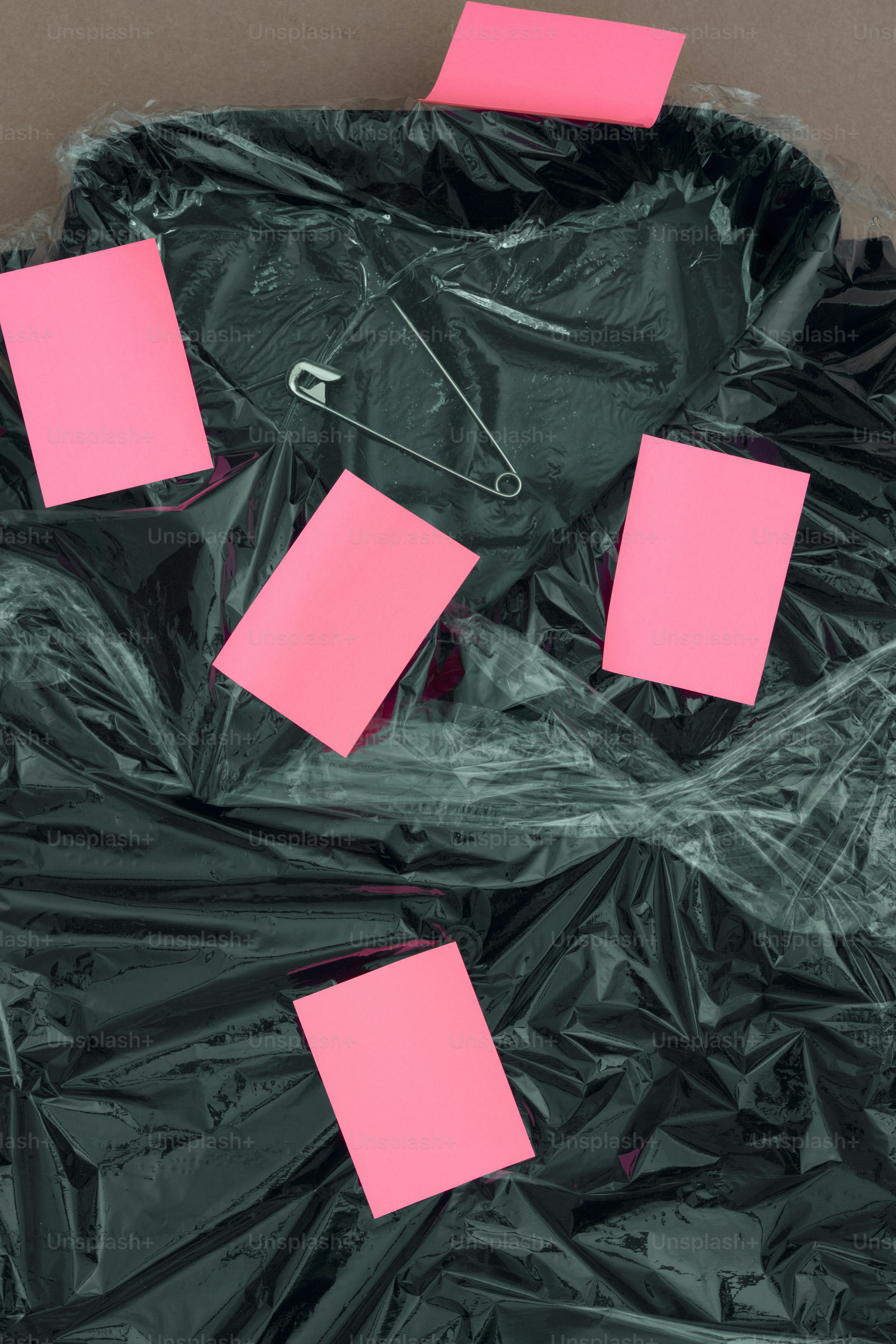 Schwarzes Kleidungsstück, in Plastik gewickelt, mit rosa Notizen und einer Nadel